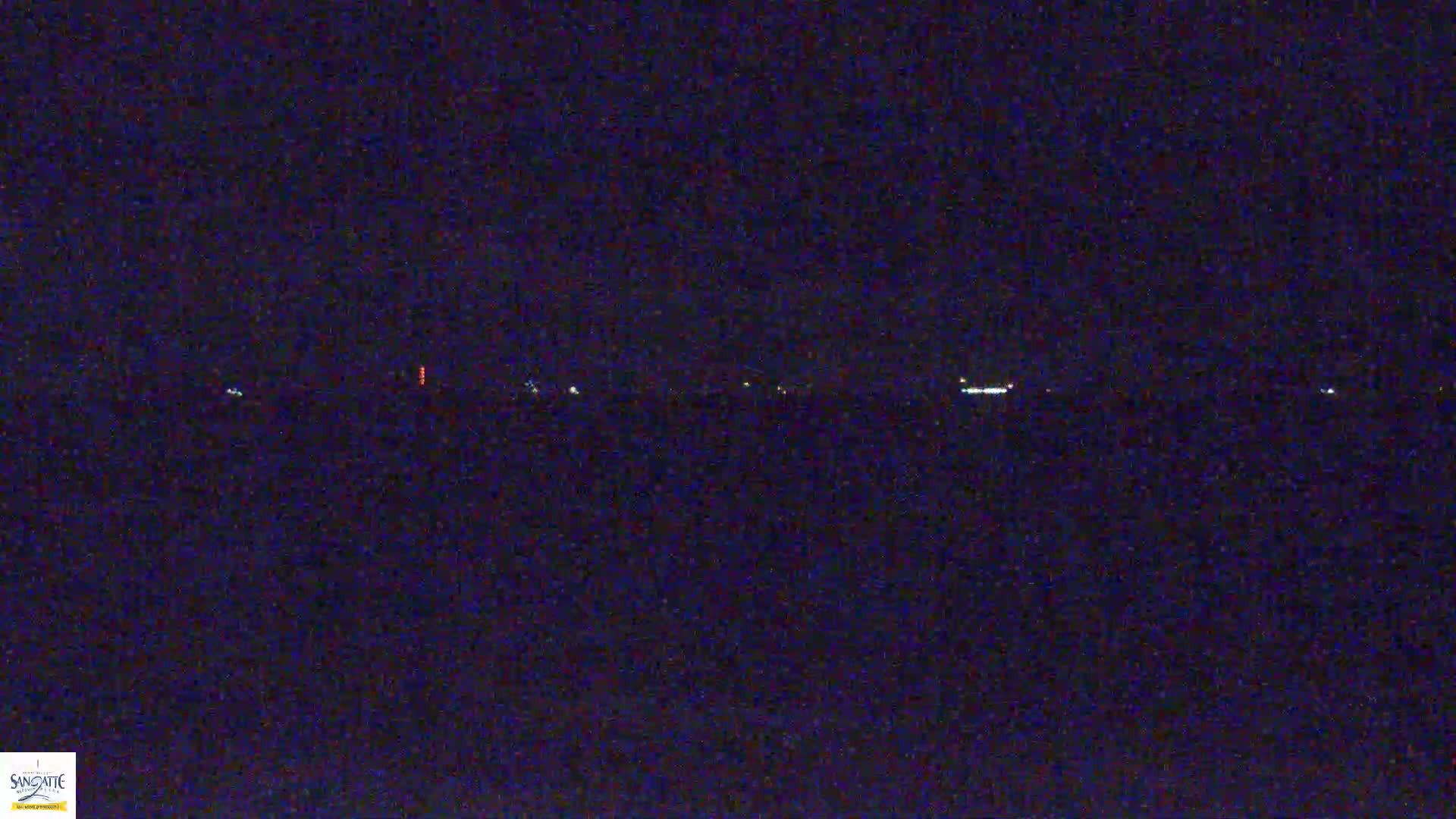 A dark, nighttime scene shows a line of faint, distant lights on the horizon.