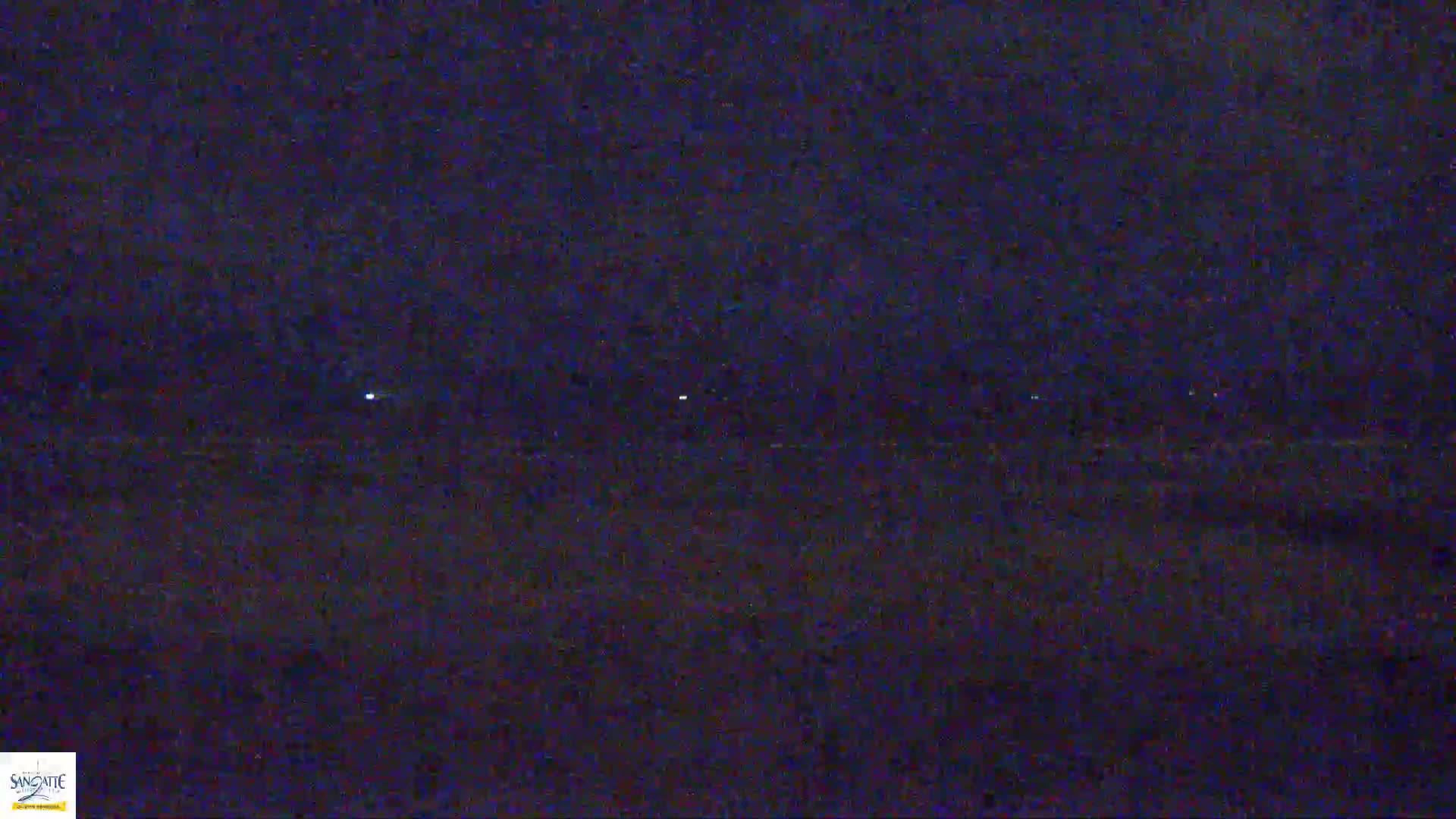 A dark, nighttime scene shows a line of faint lights in the distance on what seems to be a dark body of water or land.