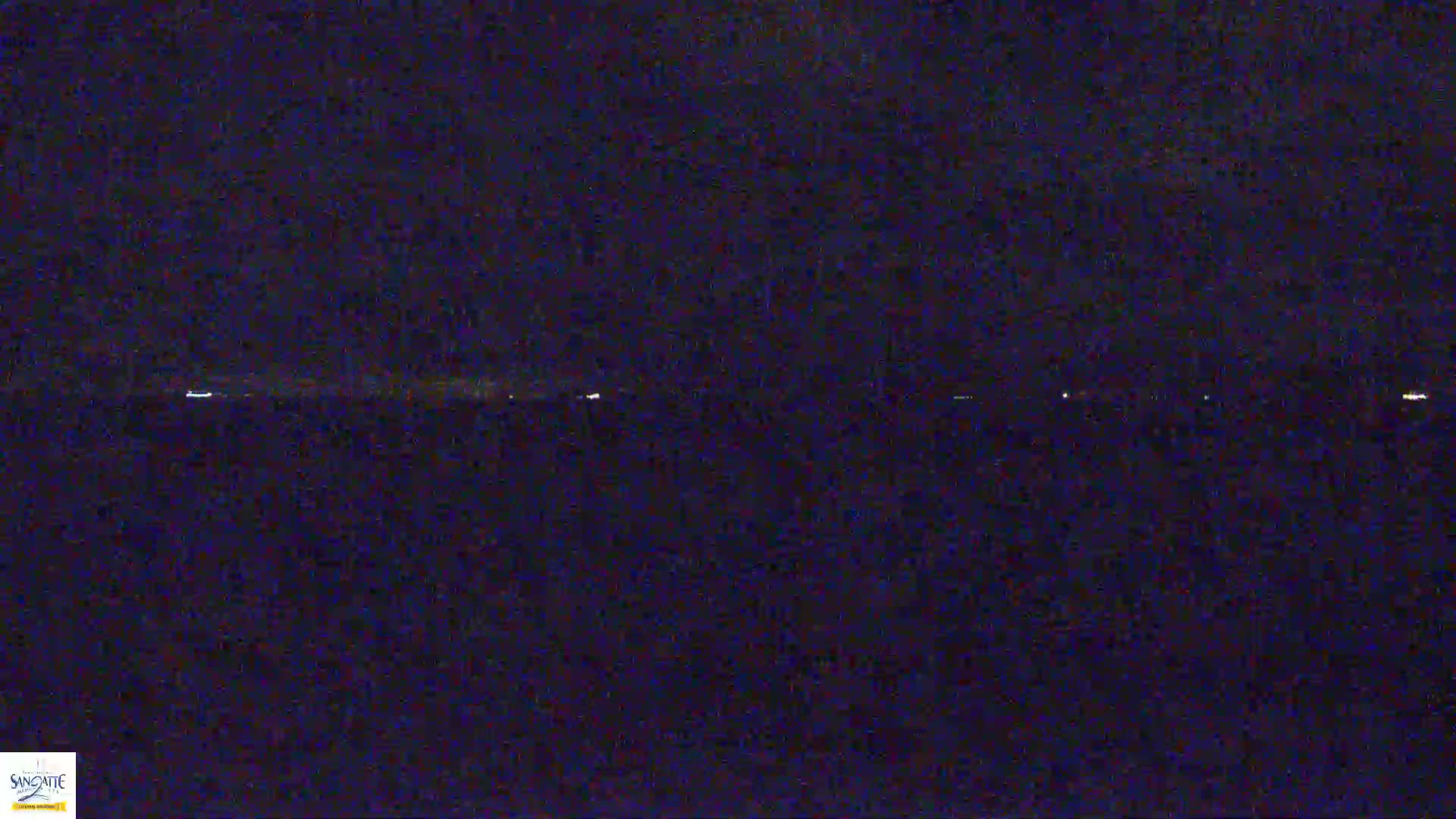 A dark, nighttime scene shows a faint line of distant lights on the horizon.