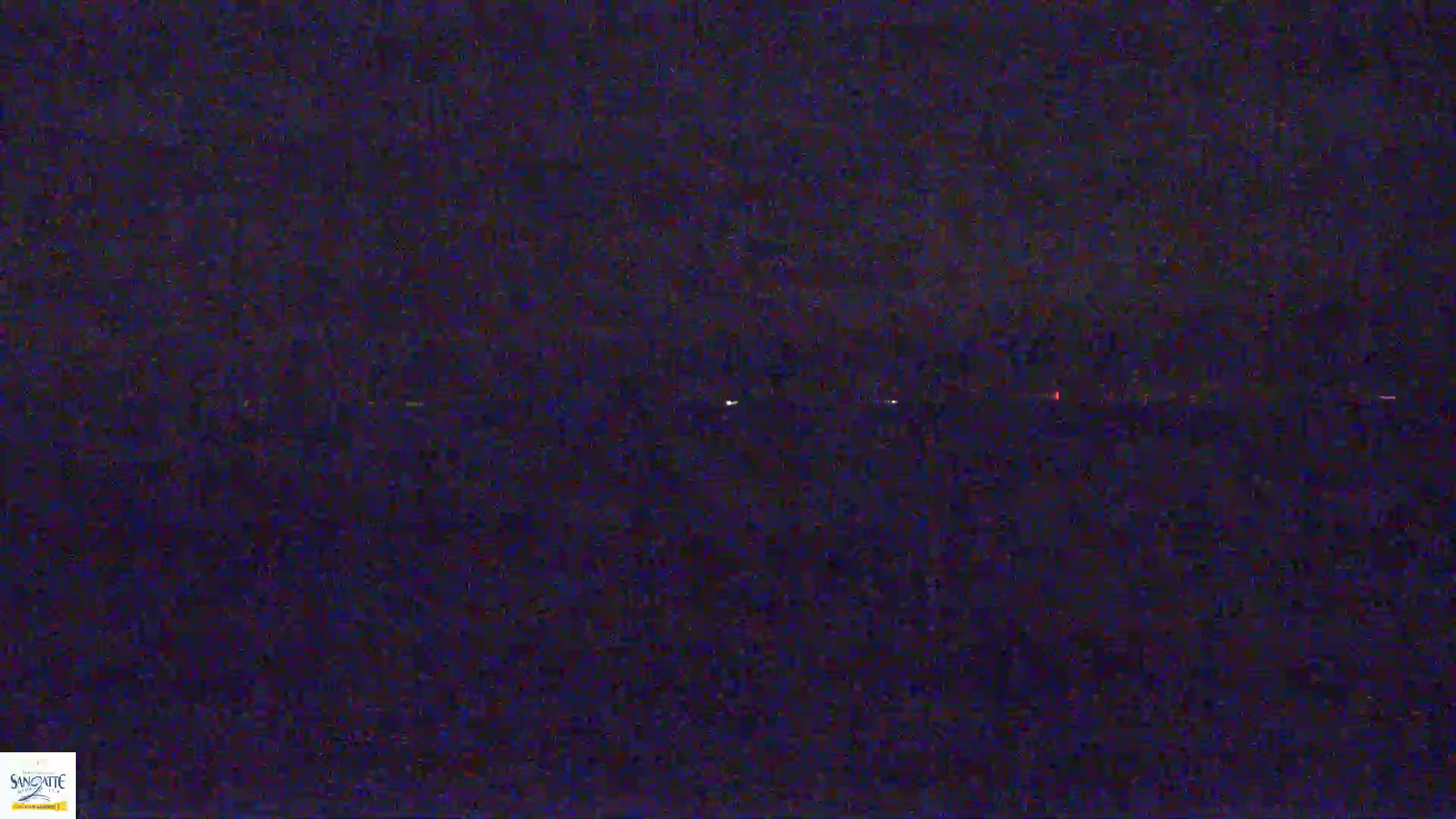 A dark, nighttime scene shows a faint horizon line with a few distant, small lights.