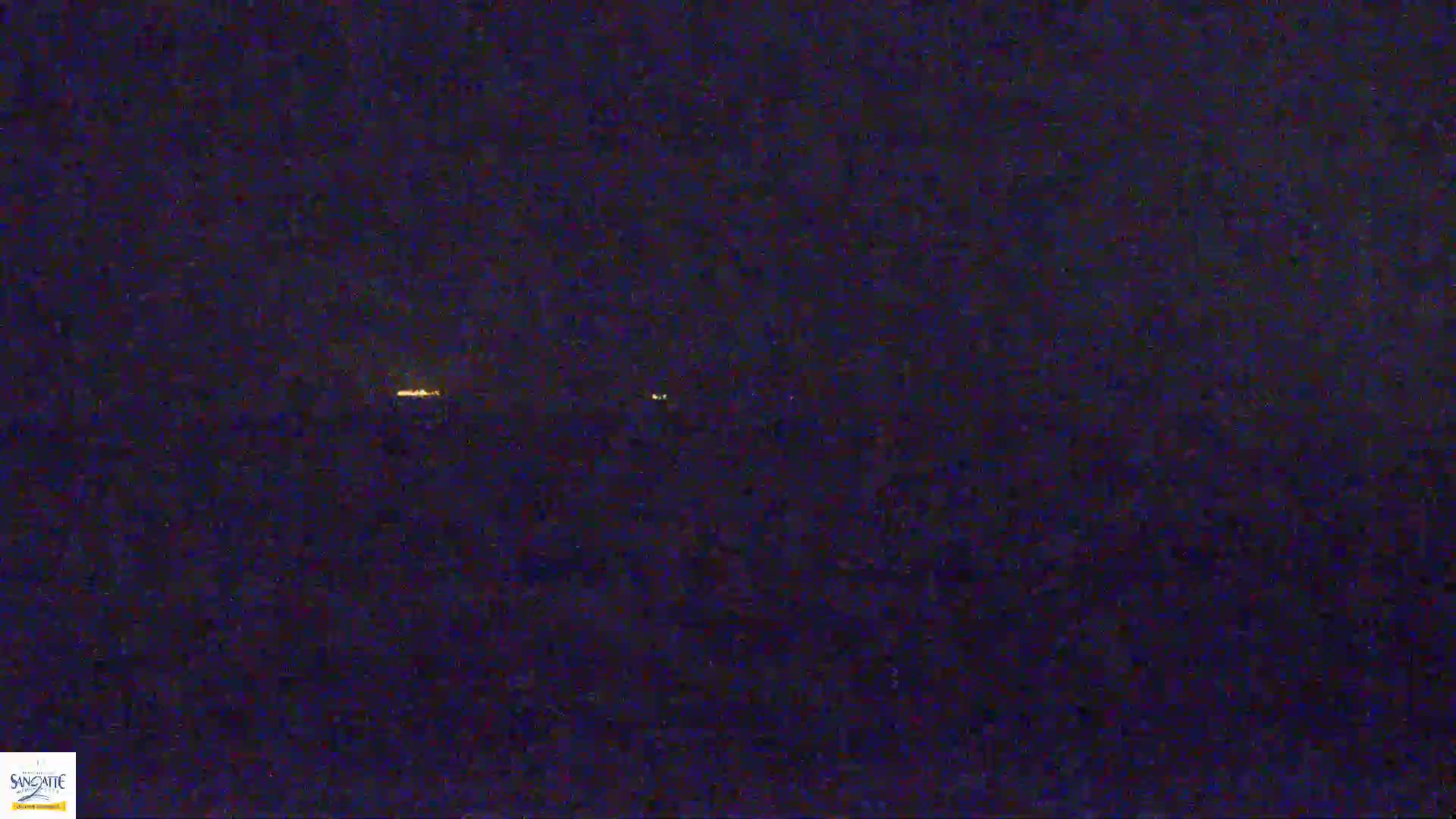 A nighttime image shows a dark landscape with a few faint, distant lights.