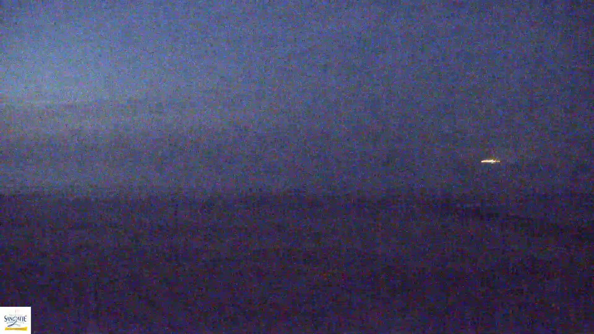 A distant, small light is visible in a dark, hazy sky over a dark, flat landscape at night.