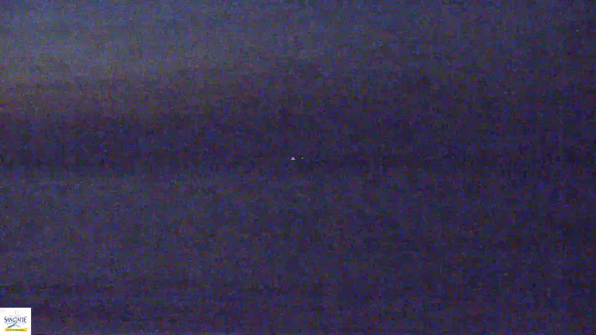 A dark, blurry image shows a body of water at night with two small, distant lights visible on the surface.