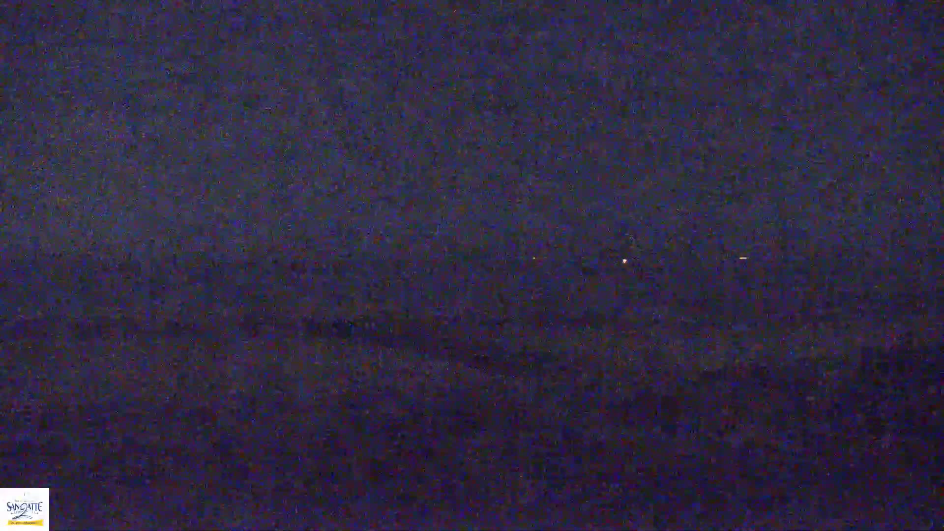 A dark, nighttime landscape is visible, showing a few distant lights under a mostly clear sky.