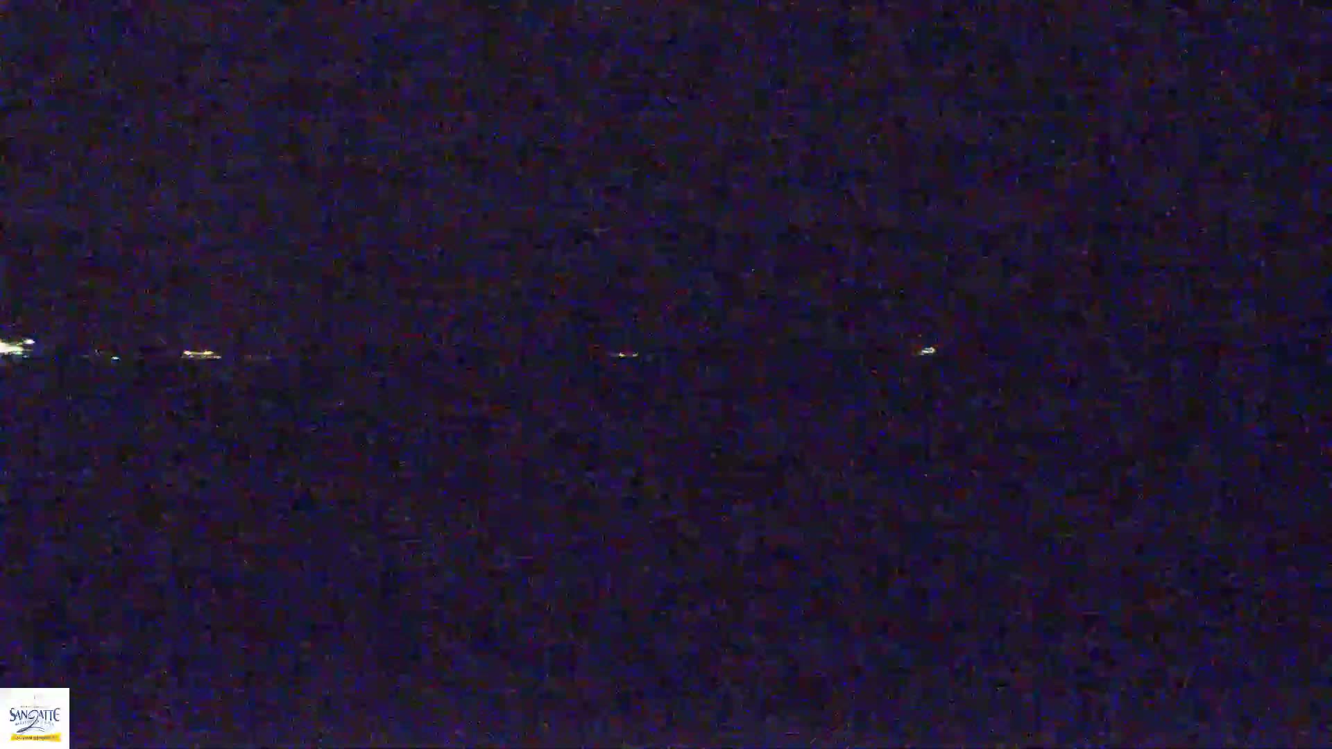 A dark, nighttime scene shows a distant line of faint lights on the horizon.
