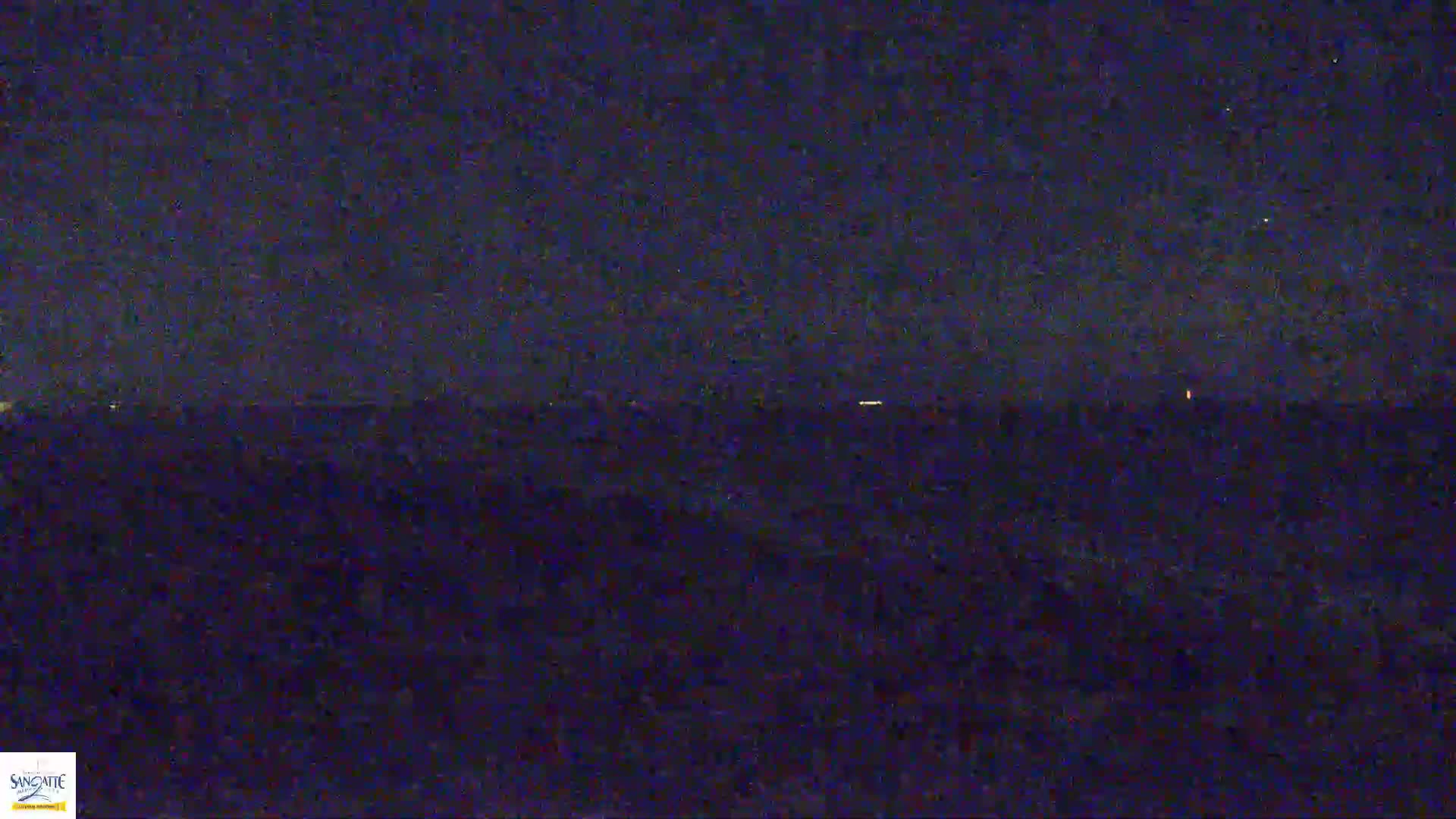 A dark, nighttime landscape is visible with a few distant lights on the horizon under a clear, dark sky.