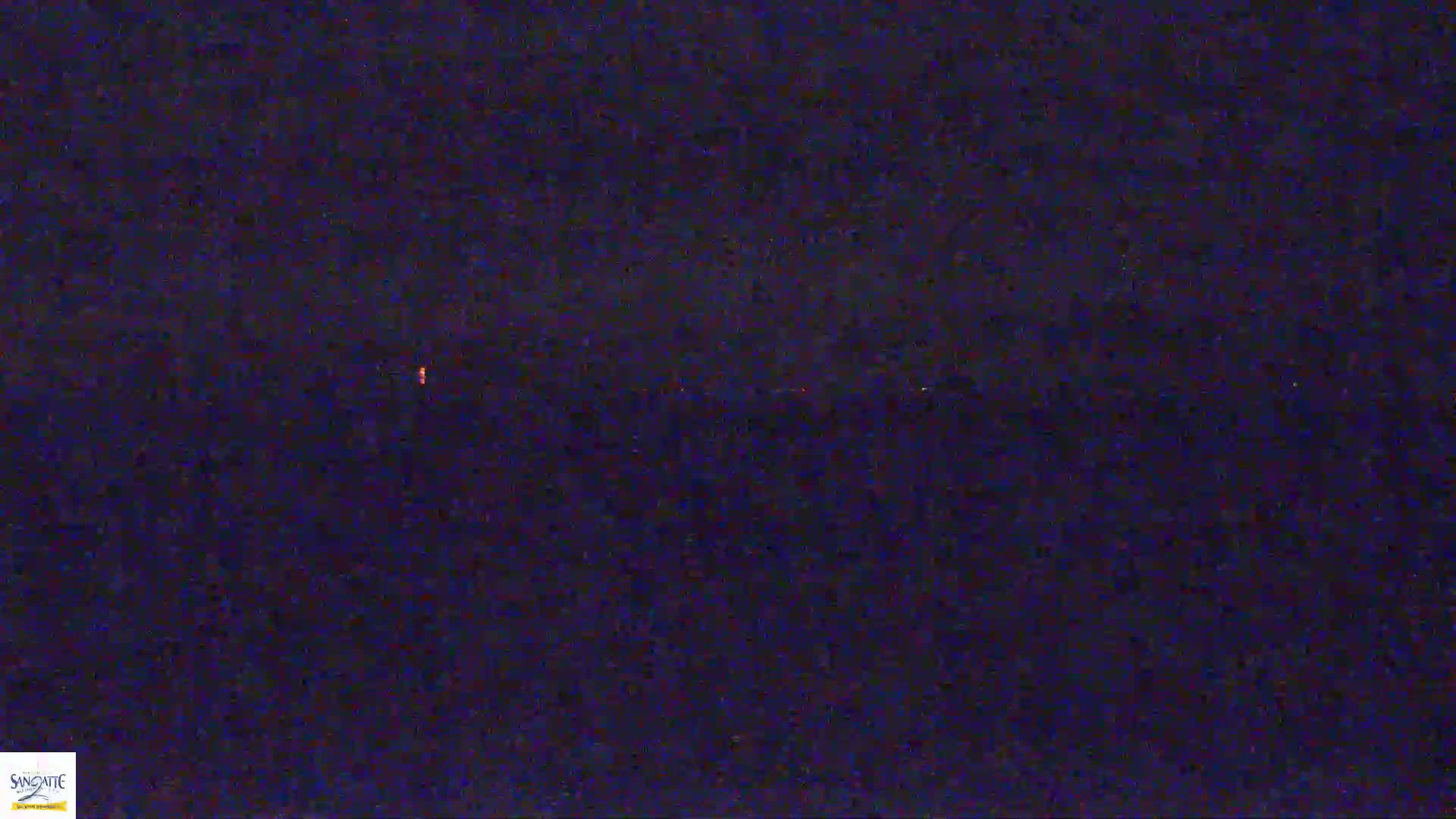 A dark, possibly nighttime, image shows a blurry, indistinct landscape with a faint orange glow in the distance.
