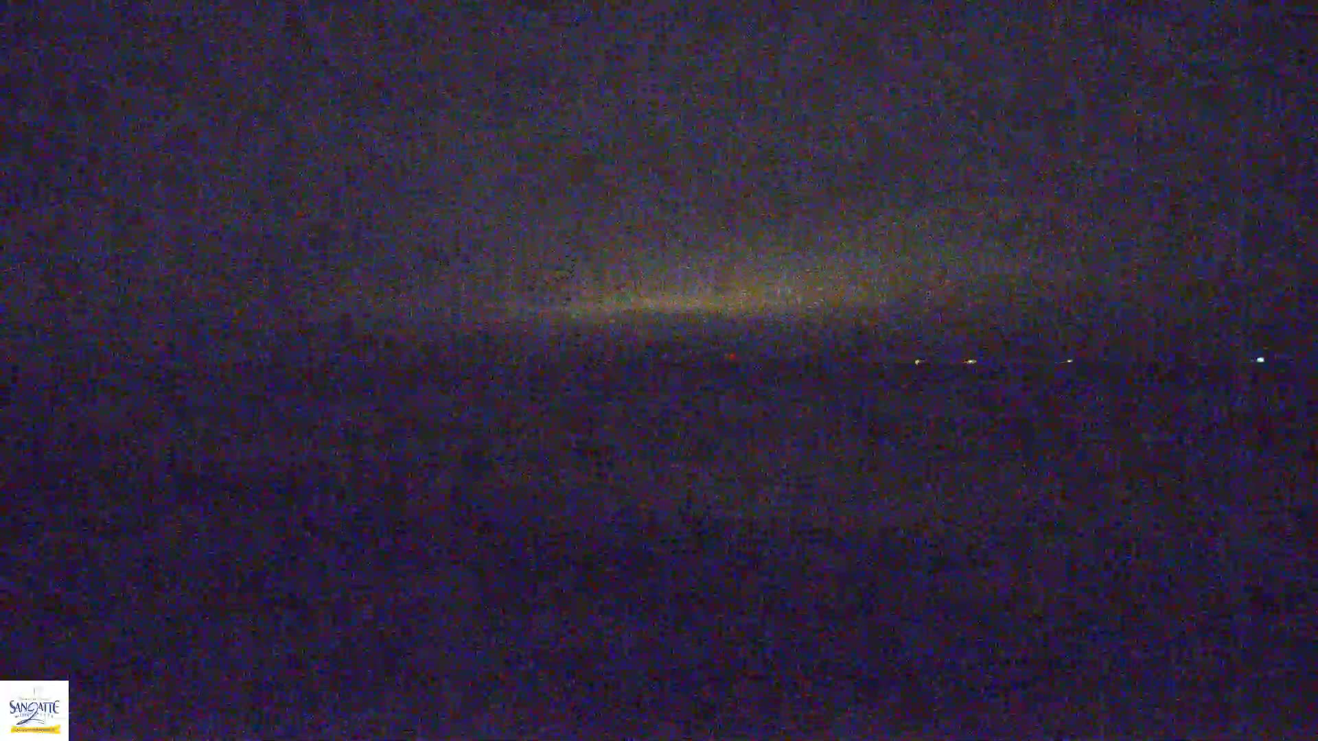 A dark, nighttime scene shows a faint, light horizon line with a few distant lights.