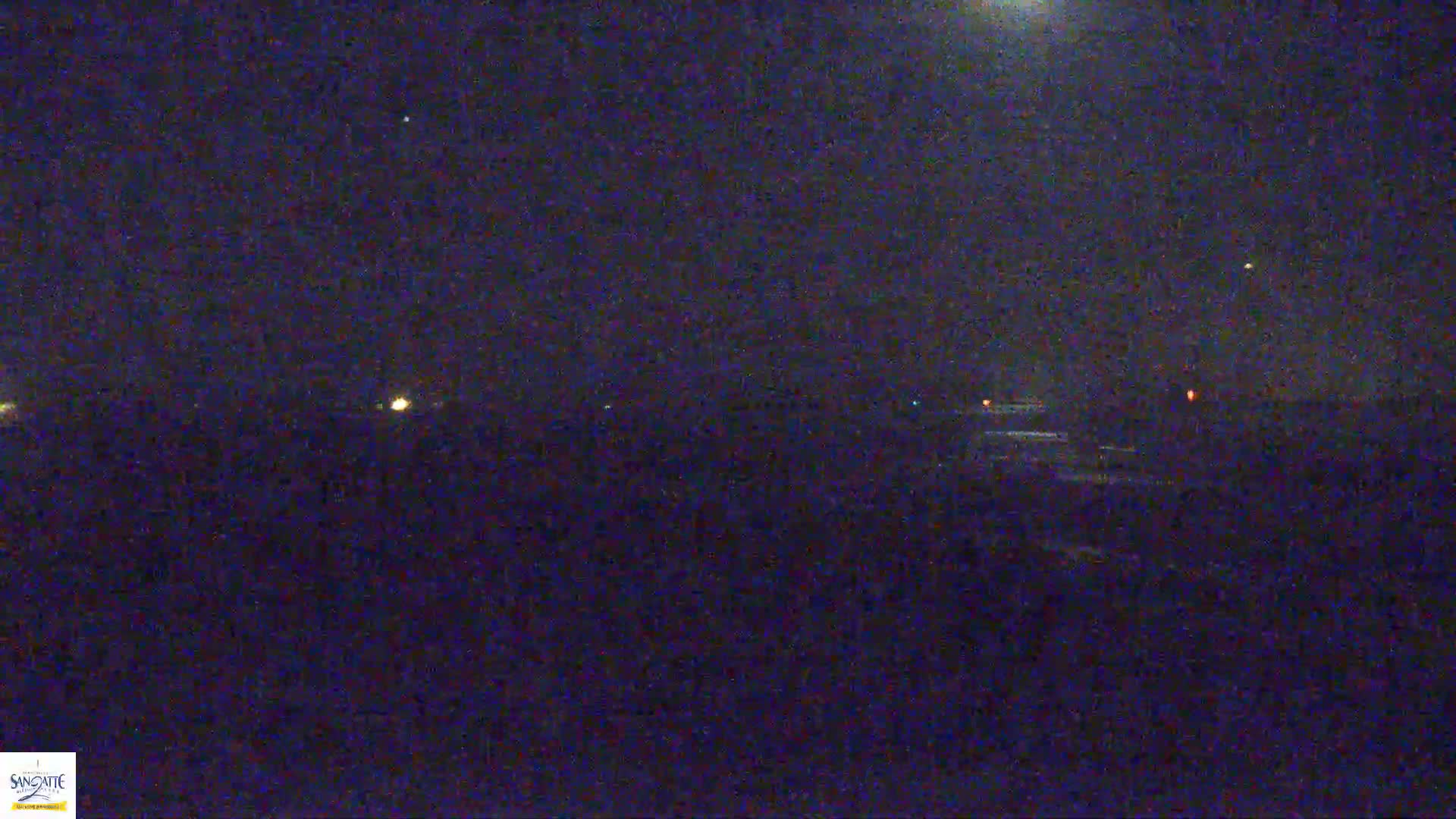 A nighttime, low-light view shows a dark landscape with a few distant, faint lights under a mostly clear, dark sky.