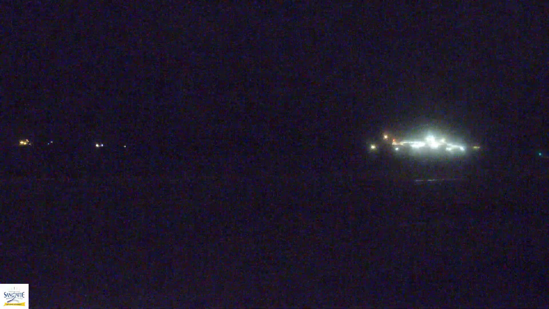 At night, several dimly lit structures are visible in the distance under a dark sky.