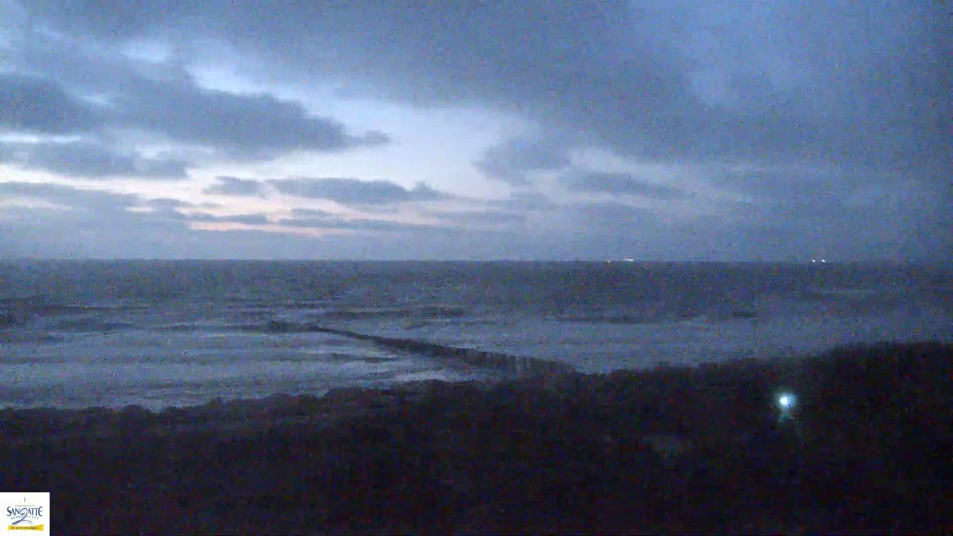 A dark, overcast sky hangs over a choppy sea, with a breakwater partially visible in the foreground.