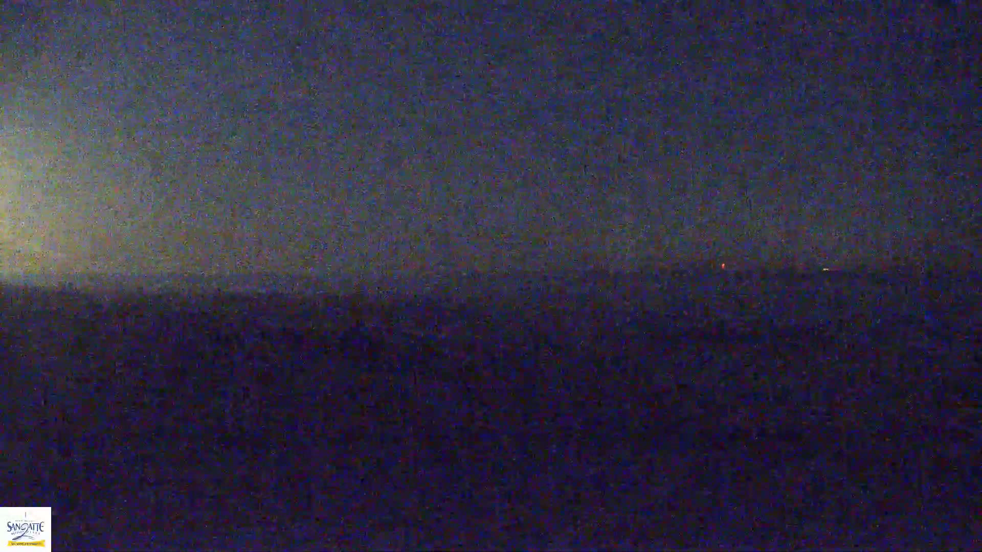 A dark, nighttime landscape is visible, with a few faint lights in the distance under a mostly clear, dark sky.