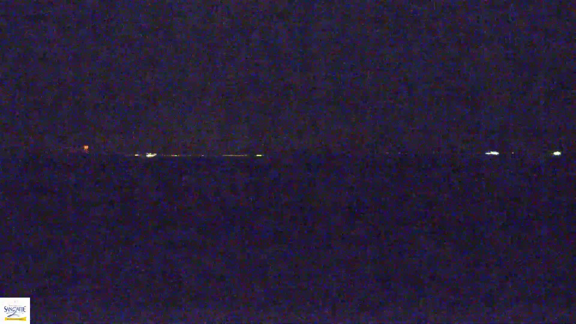 A nighttime view of a dark body of water with a line of faint lights on the horizon.