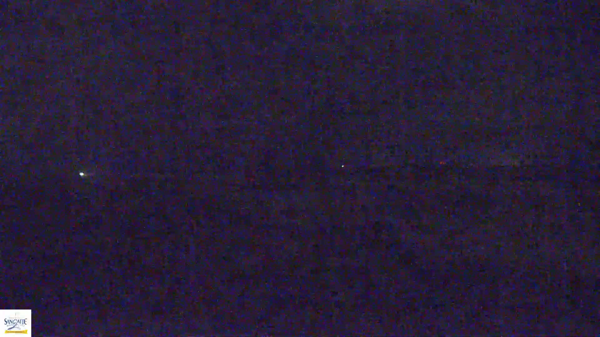 A dark, nighttime scene shows a few faint lights in the distance, possibly on the horizon.