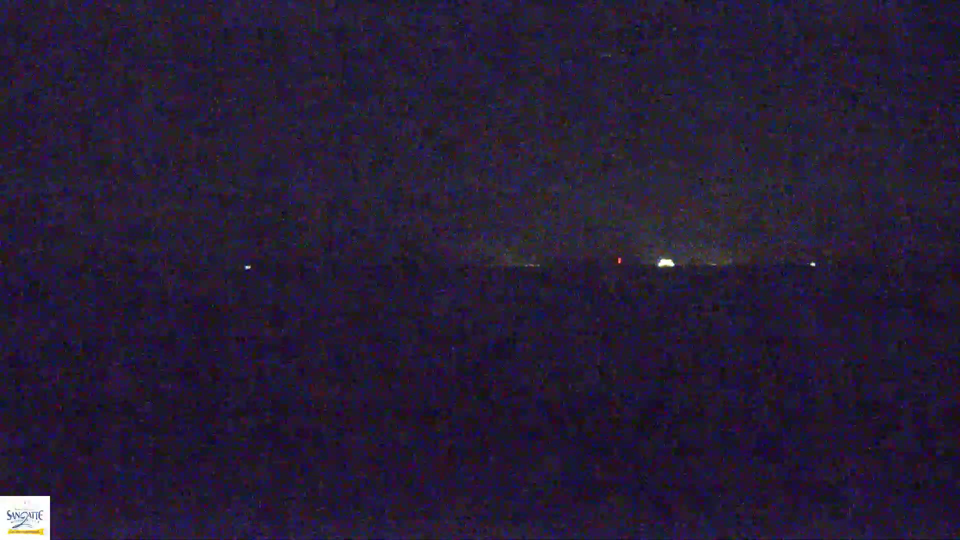 A dark, nighttime landscape is visible, with a few faint lights in the distance under a mostly clear sky.