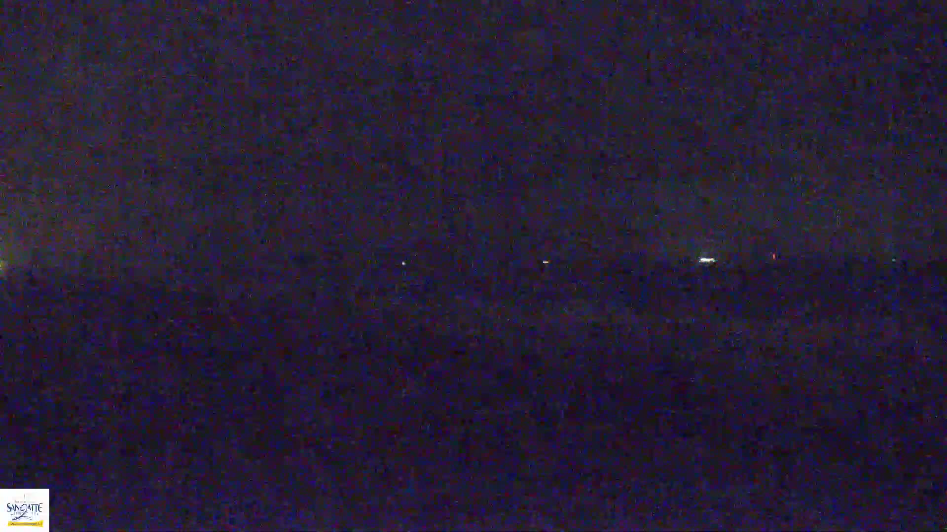 A dark, nighttime landscape is visible with a few faint lights in the distance under a mostly clear sky.