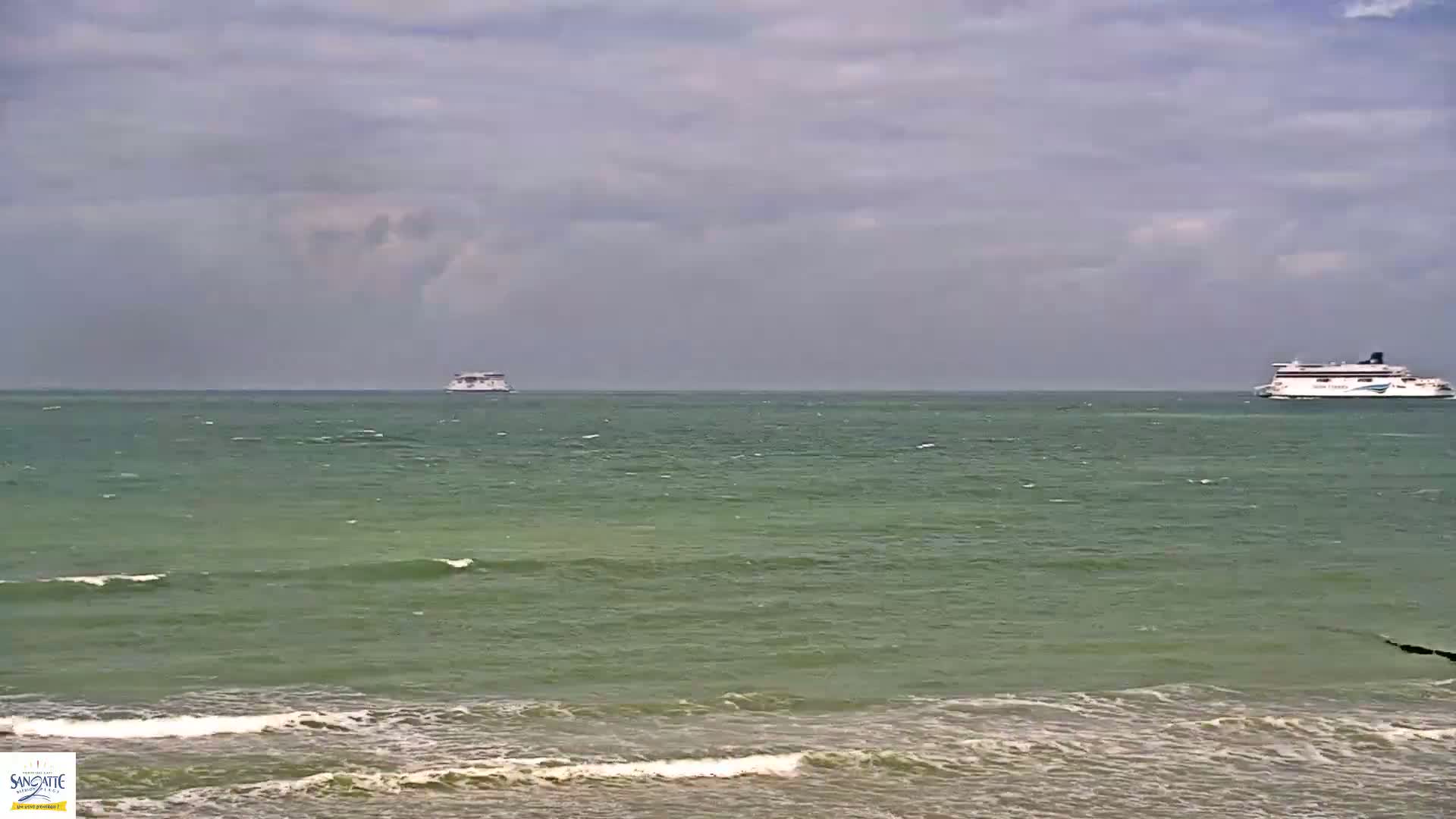 Two ferries are visible on a somewhat choppy, green-tinged ocean under a cloudy sky.