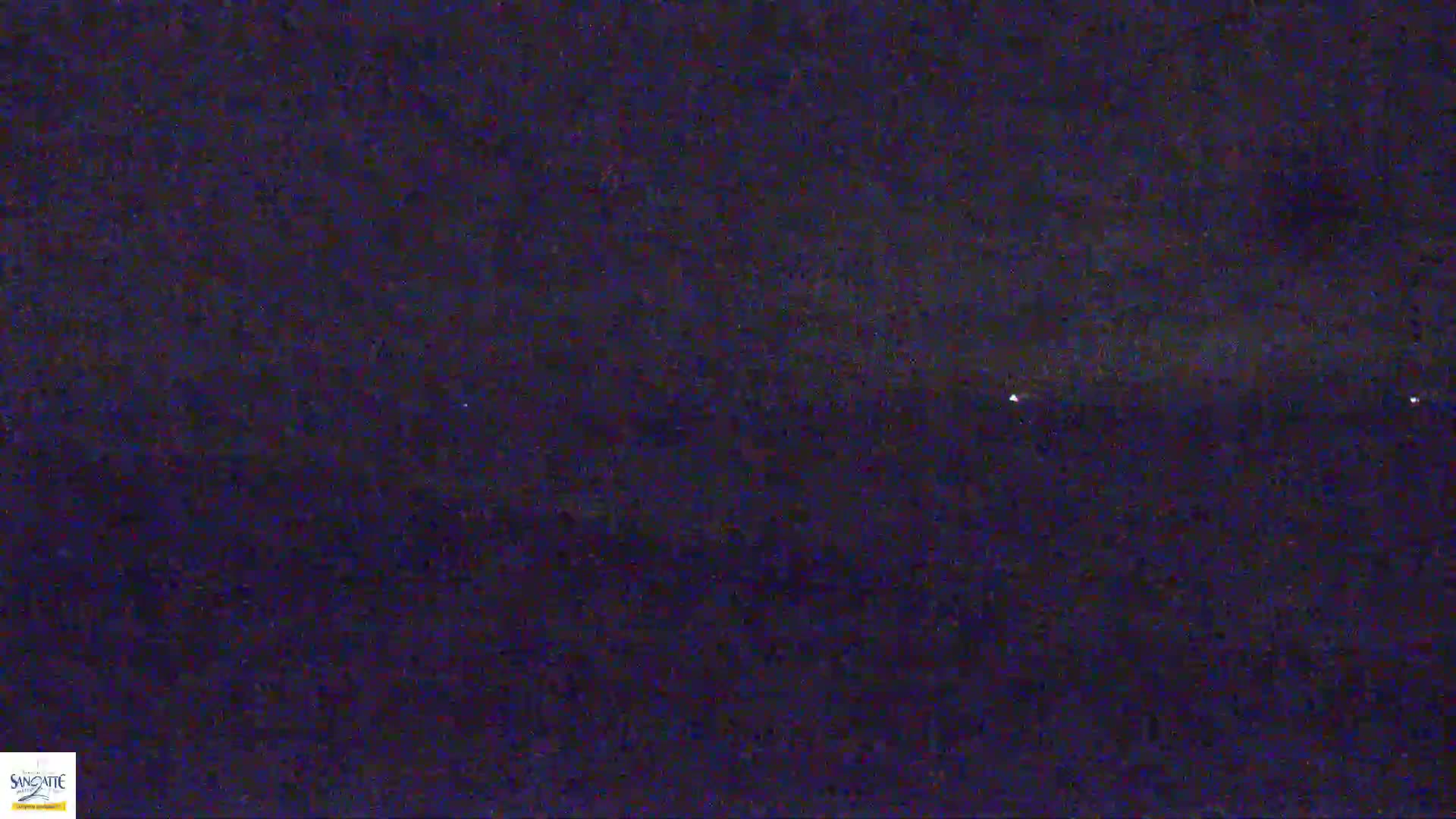 A nighttime, dark-blue, grainy image shows a few faint lights in the distance on the horizon.