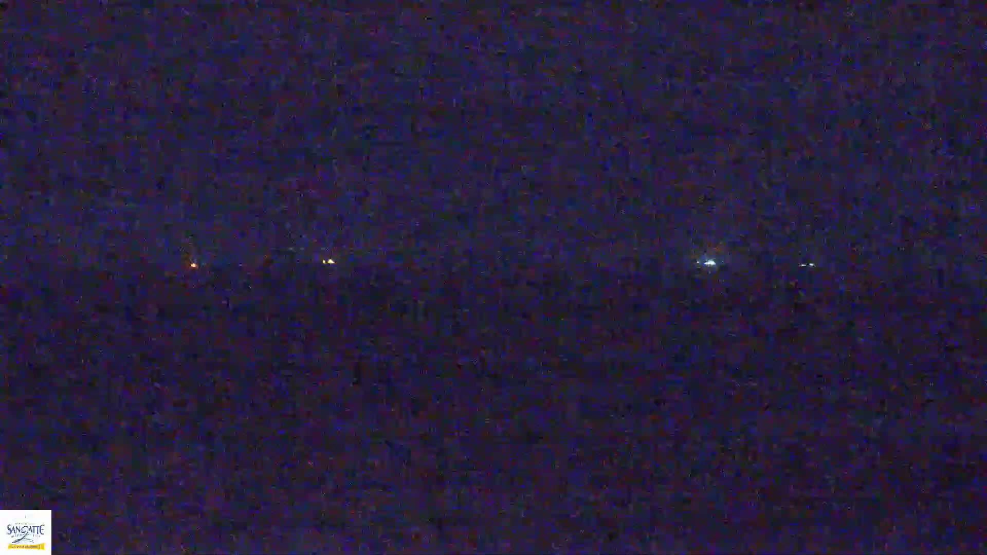 A dark, nighttime landscape shows a line of faint lights in the distance.