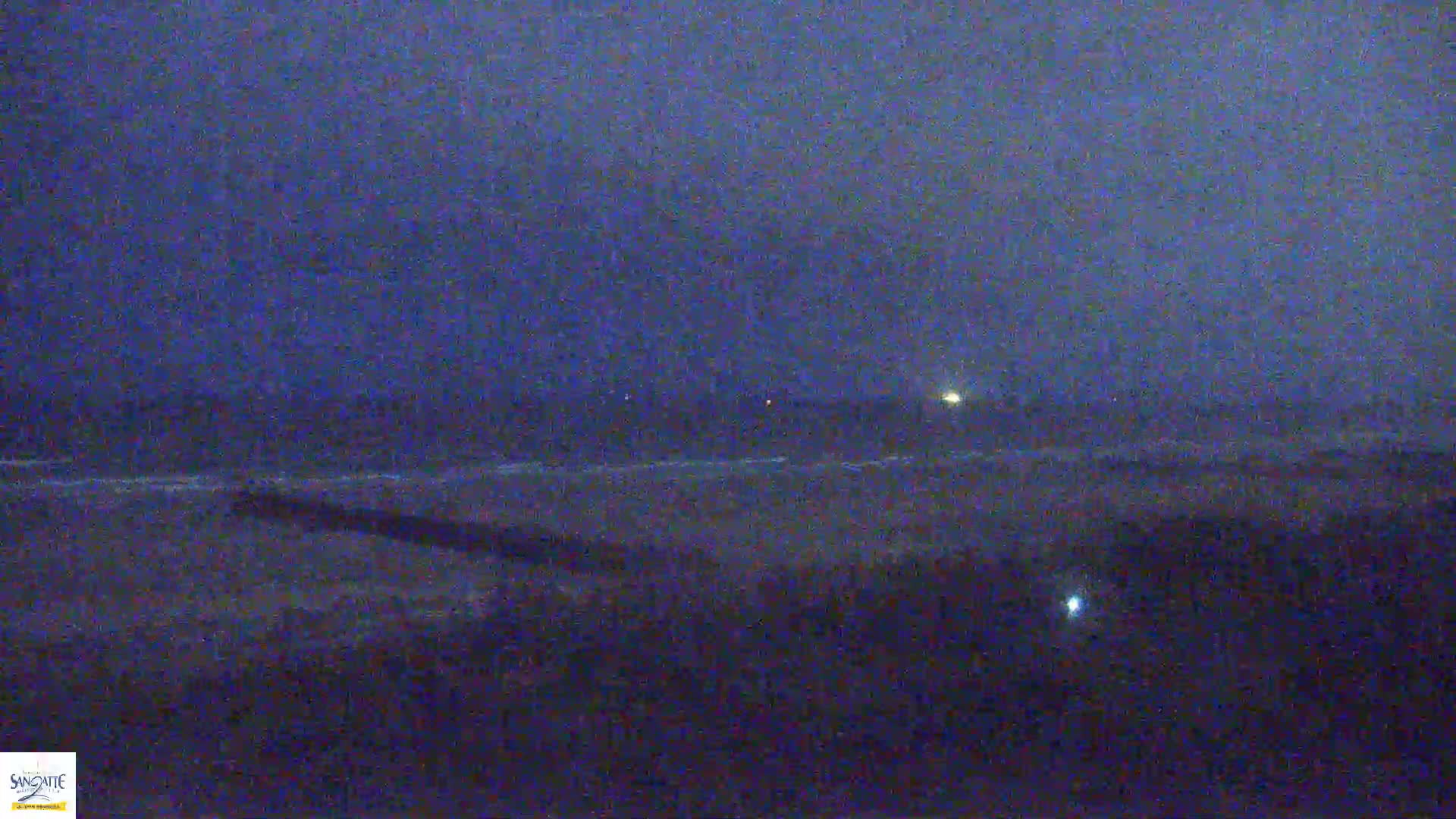 A dark, nighttime beach scene with a hazy or foggy atmosphere shows a dark ocean under a dark sky.