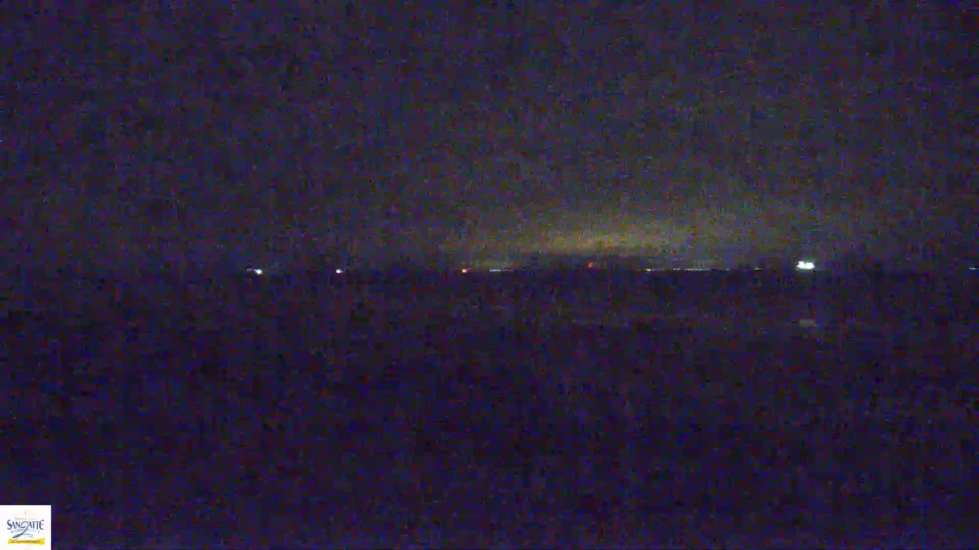 A dark, nighttime landscape is visible, showing a distant horizon with faint lights under a mostly clear sky.