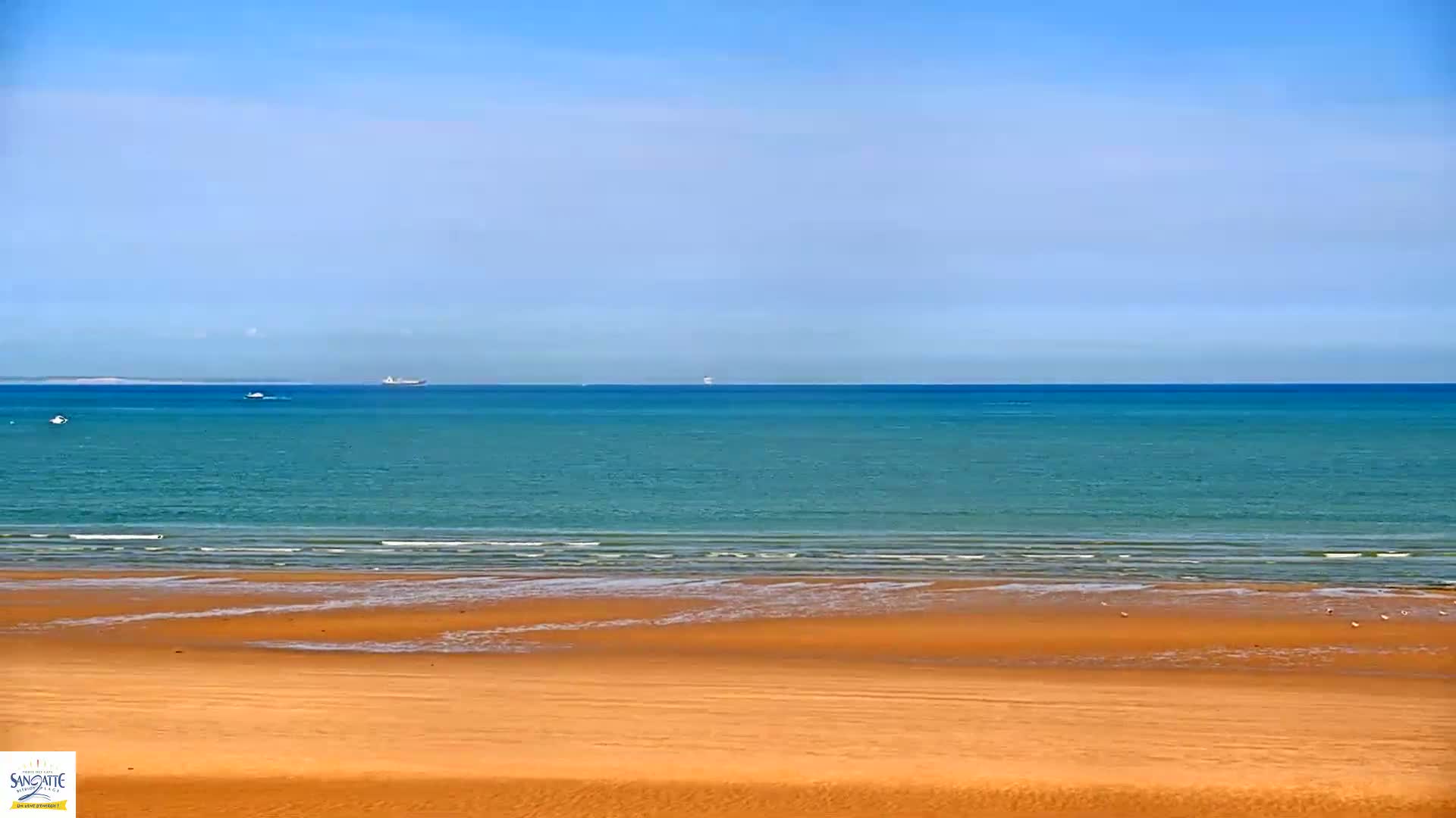 A wide sandy beach stretches to a calm teal ocean under a clear blue sky.