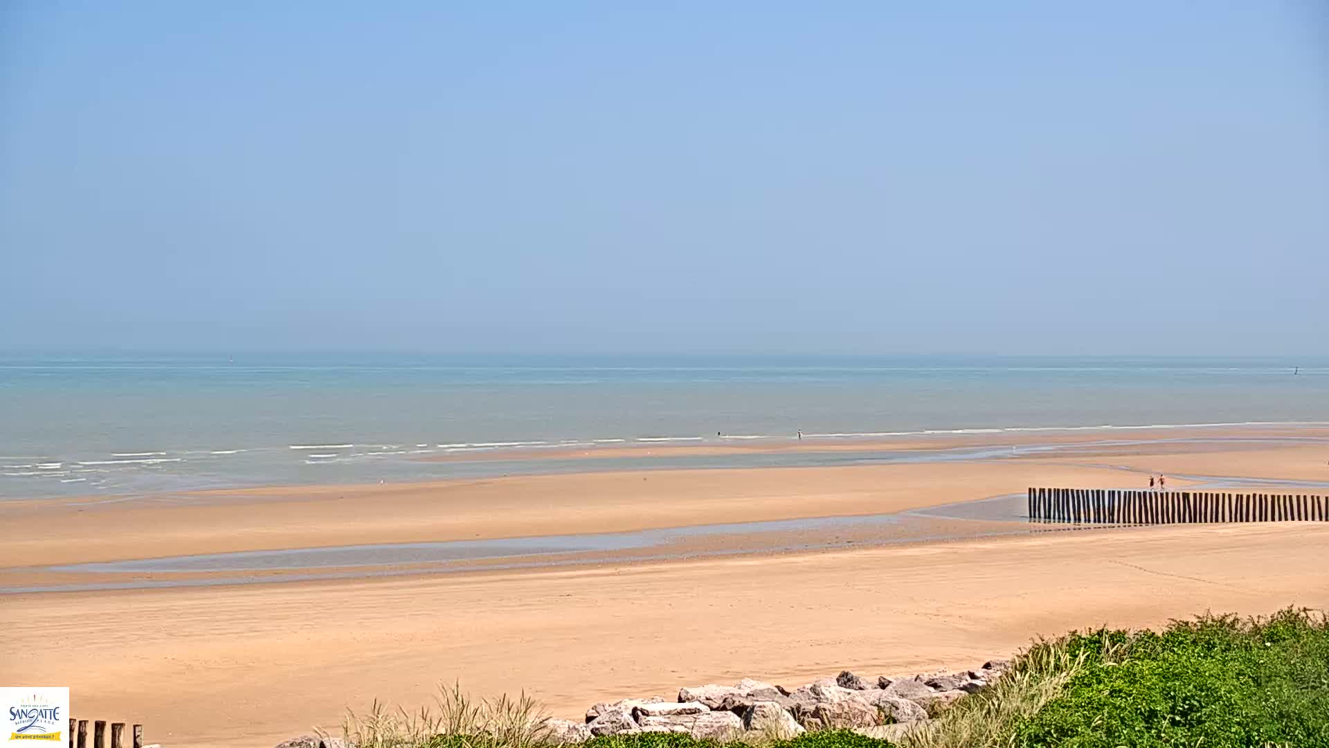 A wide sandy beach stretches to a calm, light-blue ocean under a clear blue sky.