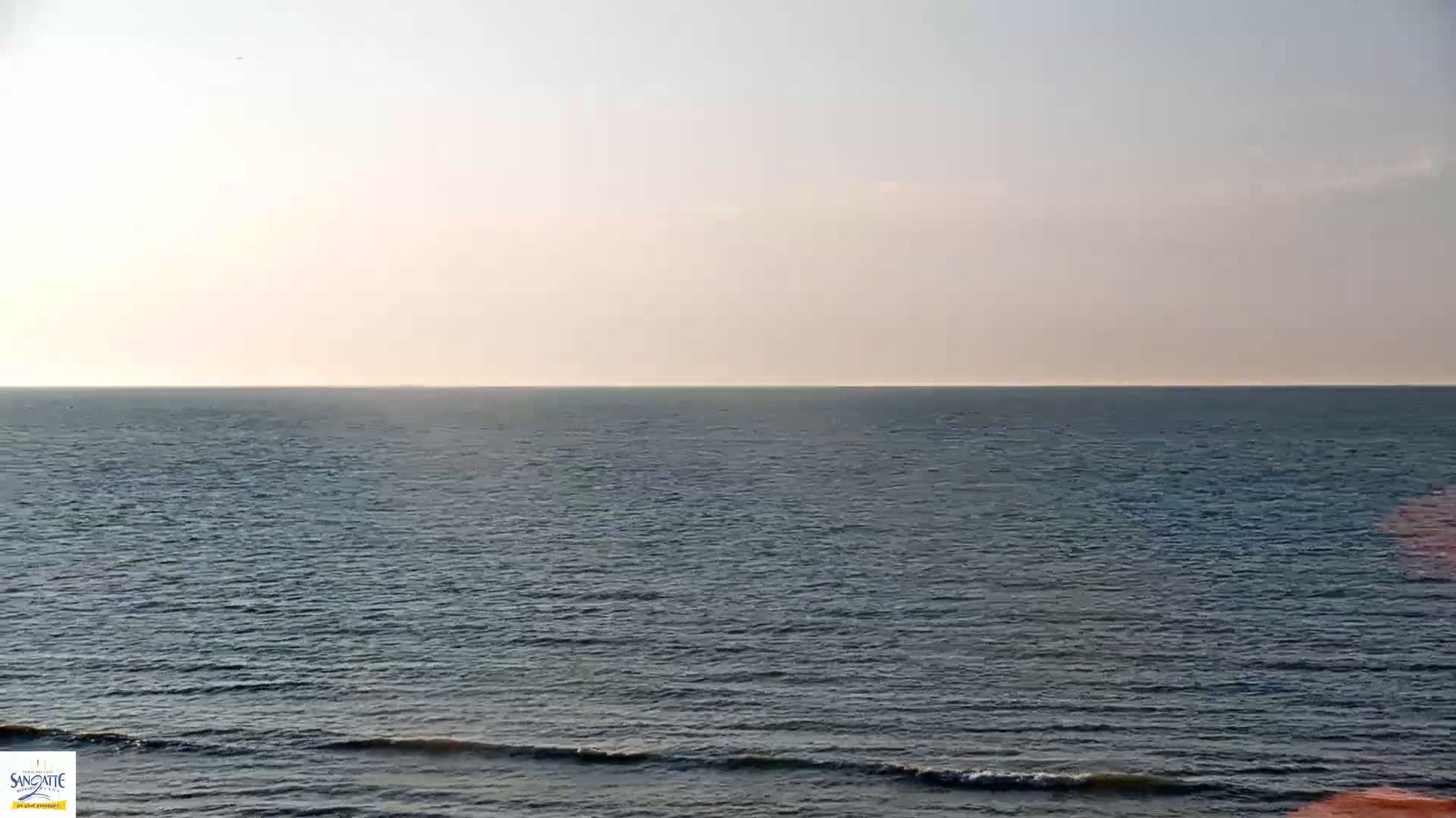 A calm, gray-blue ocean stretches to a pale horizon under a mostly clear sky.
