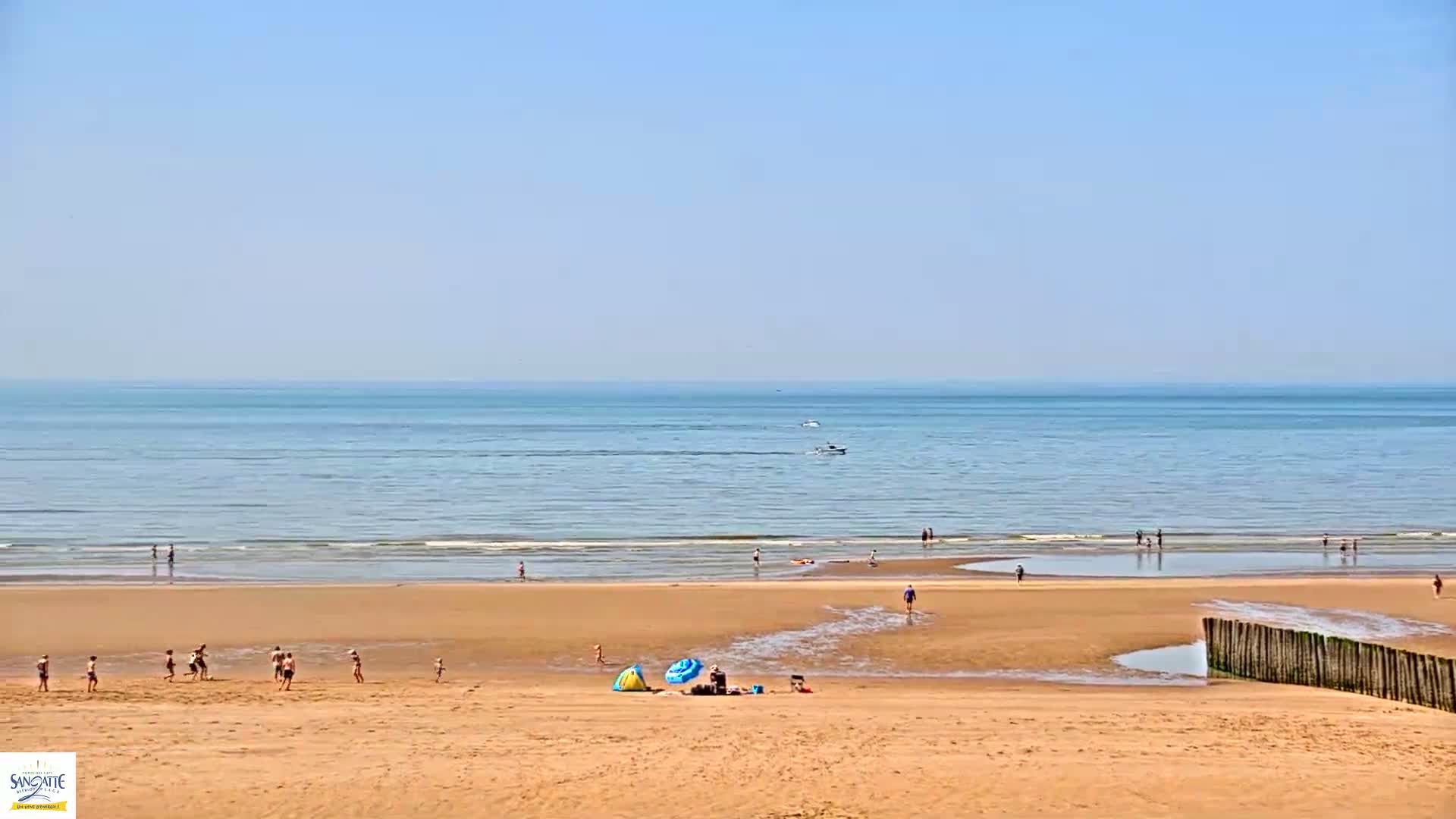 A sandy beach with scattered people enjoying a sunny day, with calm ocean waters extending to the horizon.