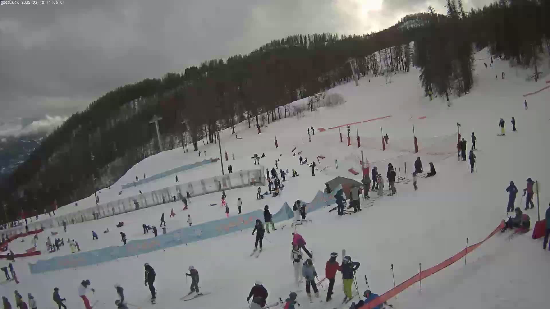 A snowy ski slope with numerous skiers and snowboarders, under an overcast sky.