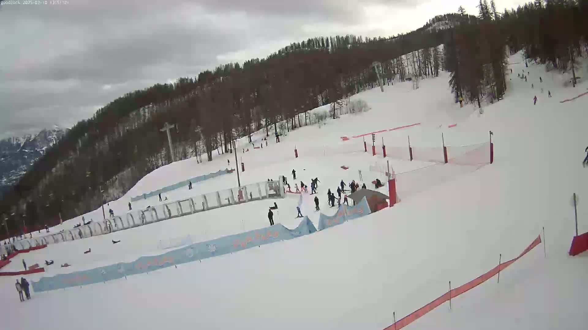 A snowy ski slope with several skiers and snowboarders, under an overcast sky.