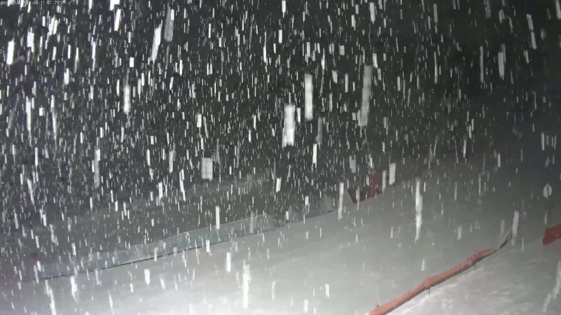 Heavy snow falls at night onto a snow-covered ground.