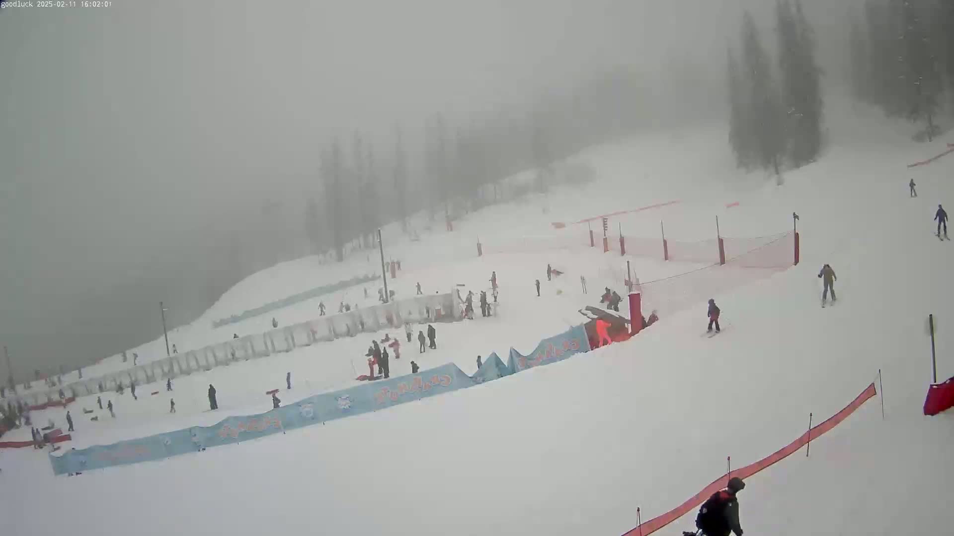 A snowy ski slope with several skiers and snowboarders visible in a heavy fog.
