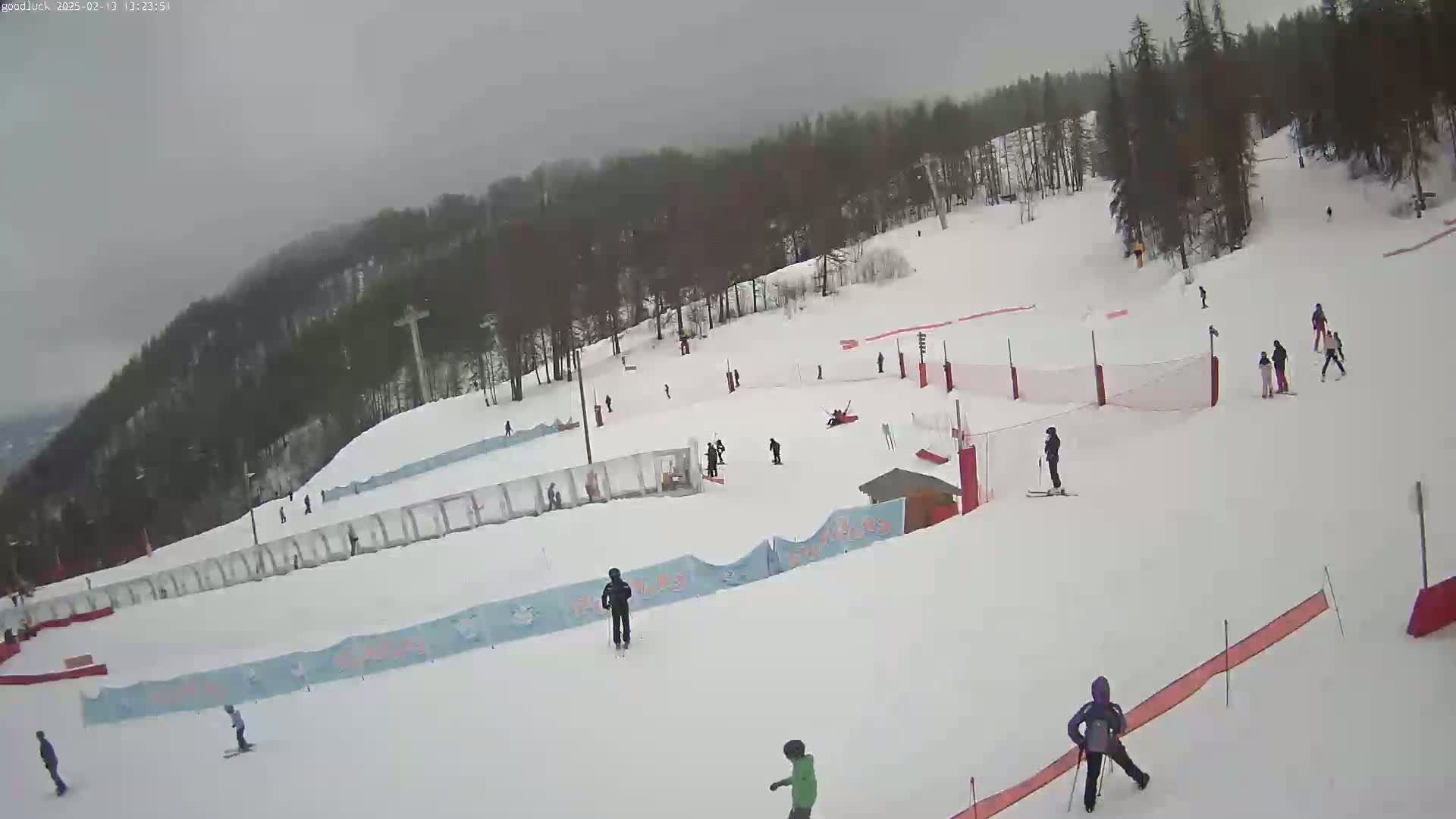 A snow-covered ski slope with several skiers and snowboarders on a cloudy day.