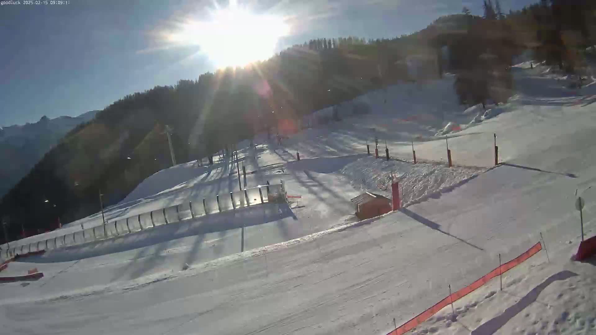A sunny, snow-covered ski slope with a lift and surrounding trees is visible.