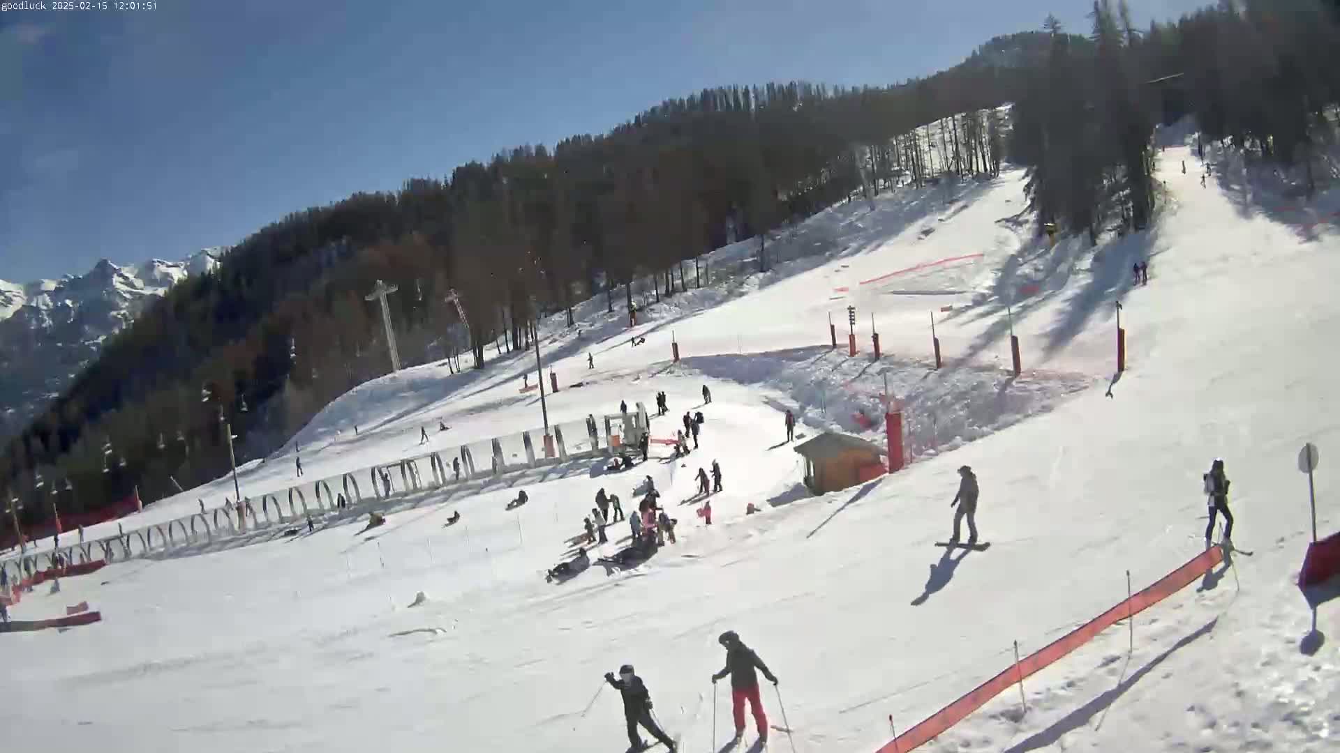 A sunny day on a snow-covered ski slope shows several skiers and snowboarders enjoying the mountain scenery.
