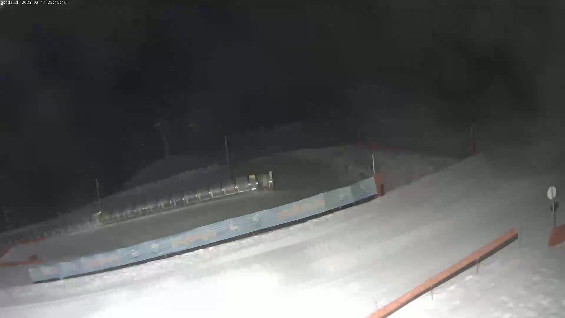 A snow-covered ski slope is visible at night, with a lift and fencing in the background.