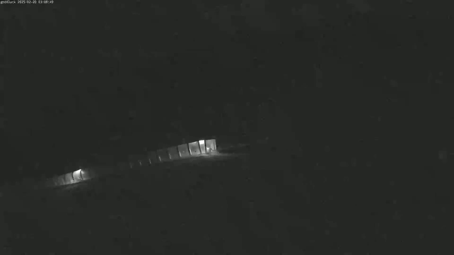 A dimly lit, nighttime scene shows a long, low structure with faint lights at either end.