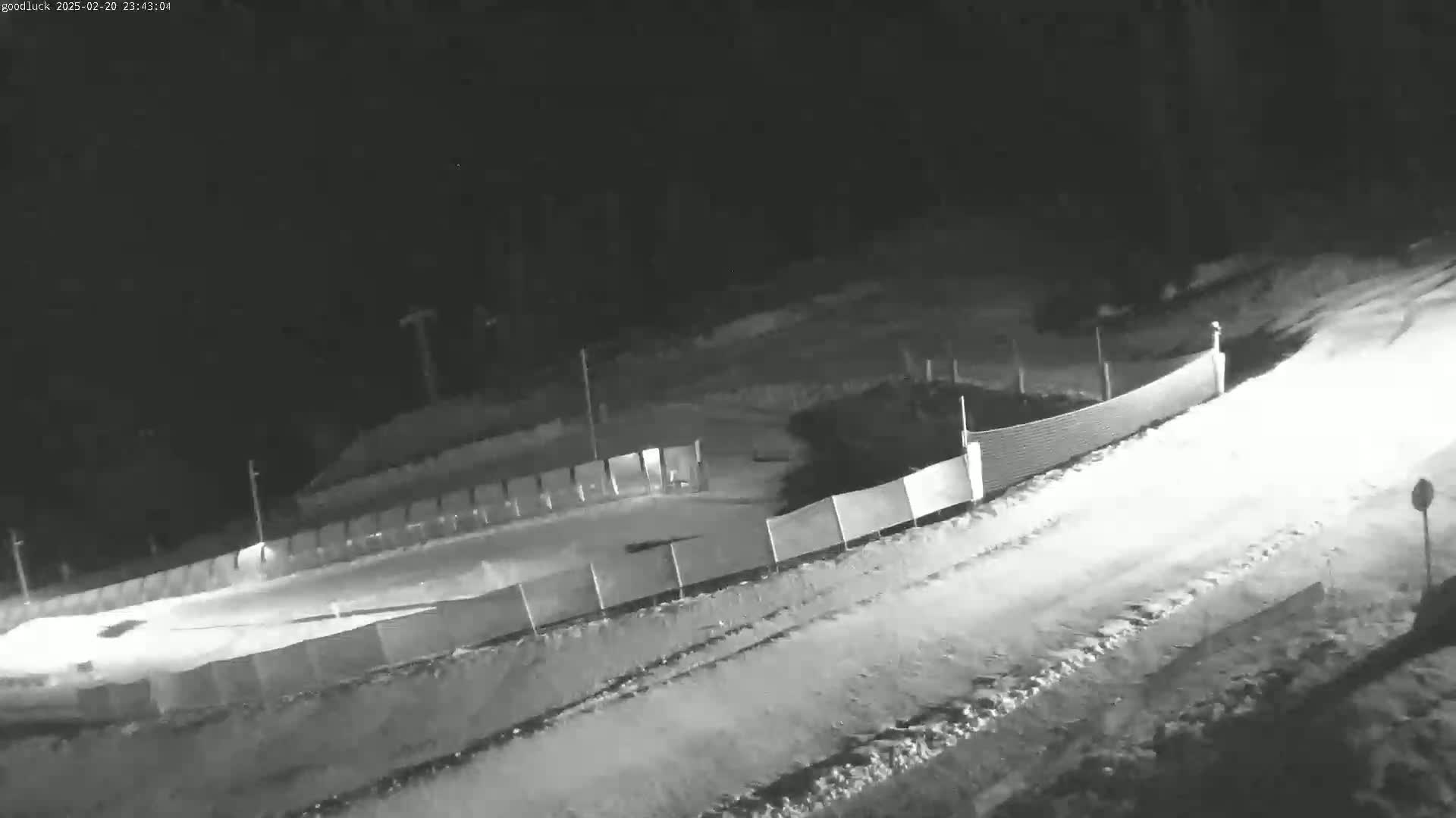 A snow-covered outdoor track or luge run is enclosed by a fence at night.