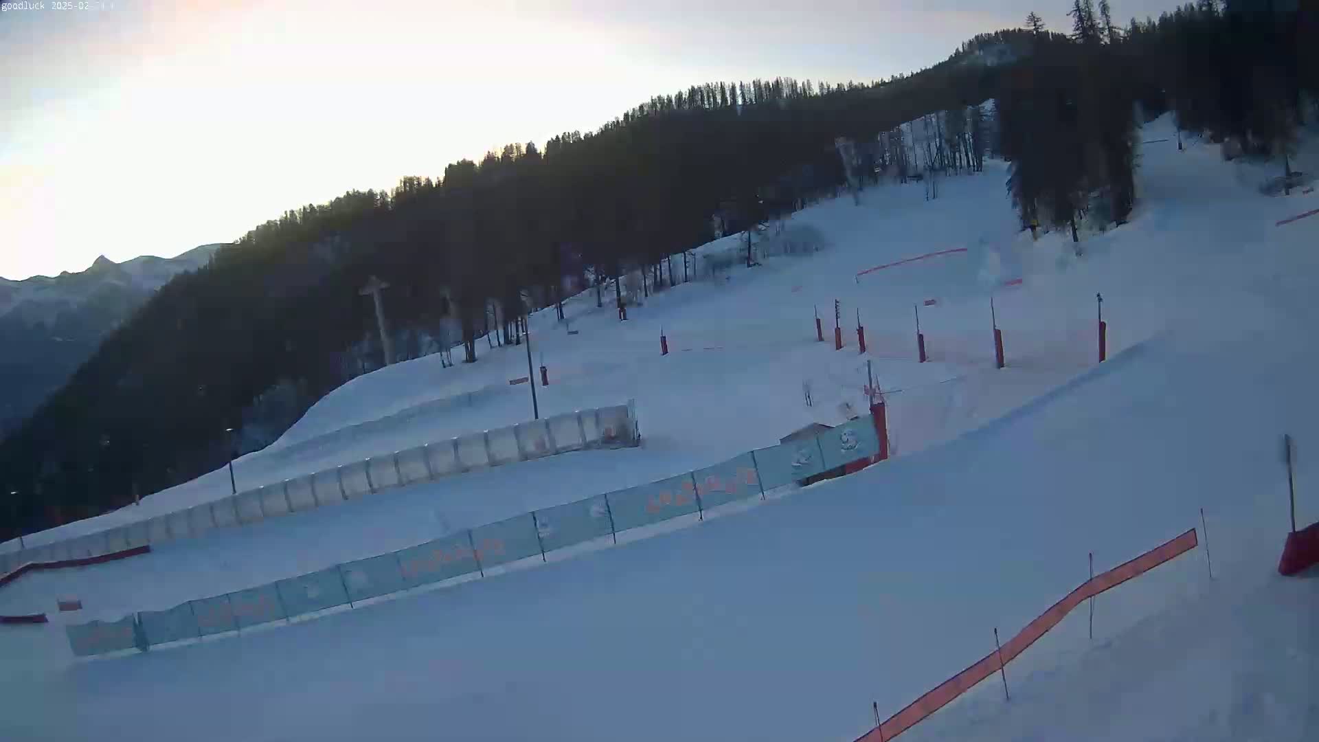 A snow-covered ski slope with trees in the background under a clear, bright sky.