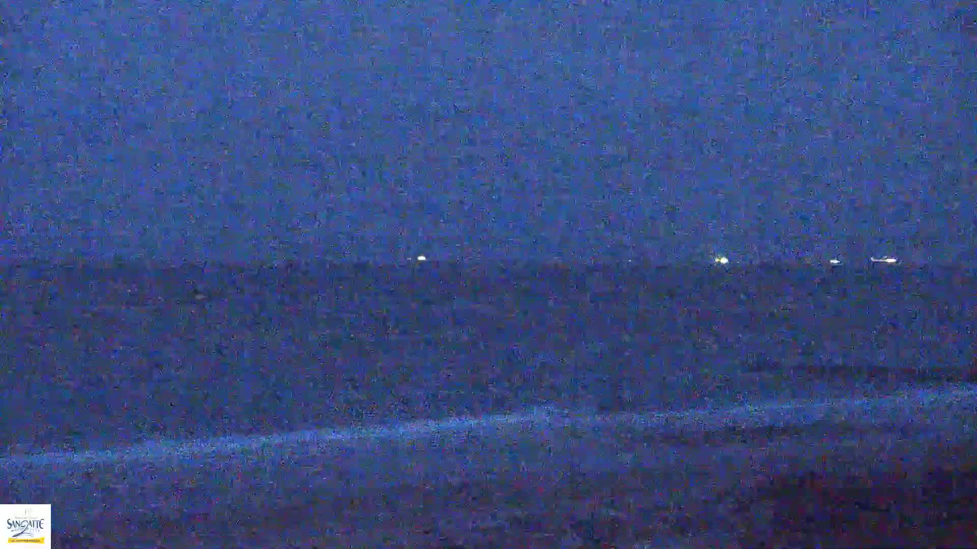 A dark, nighttime view shows a flat expanse of water with a few faint lights visible on the horizon.
