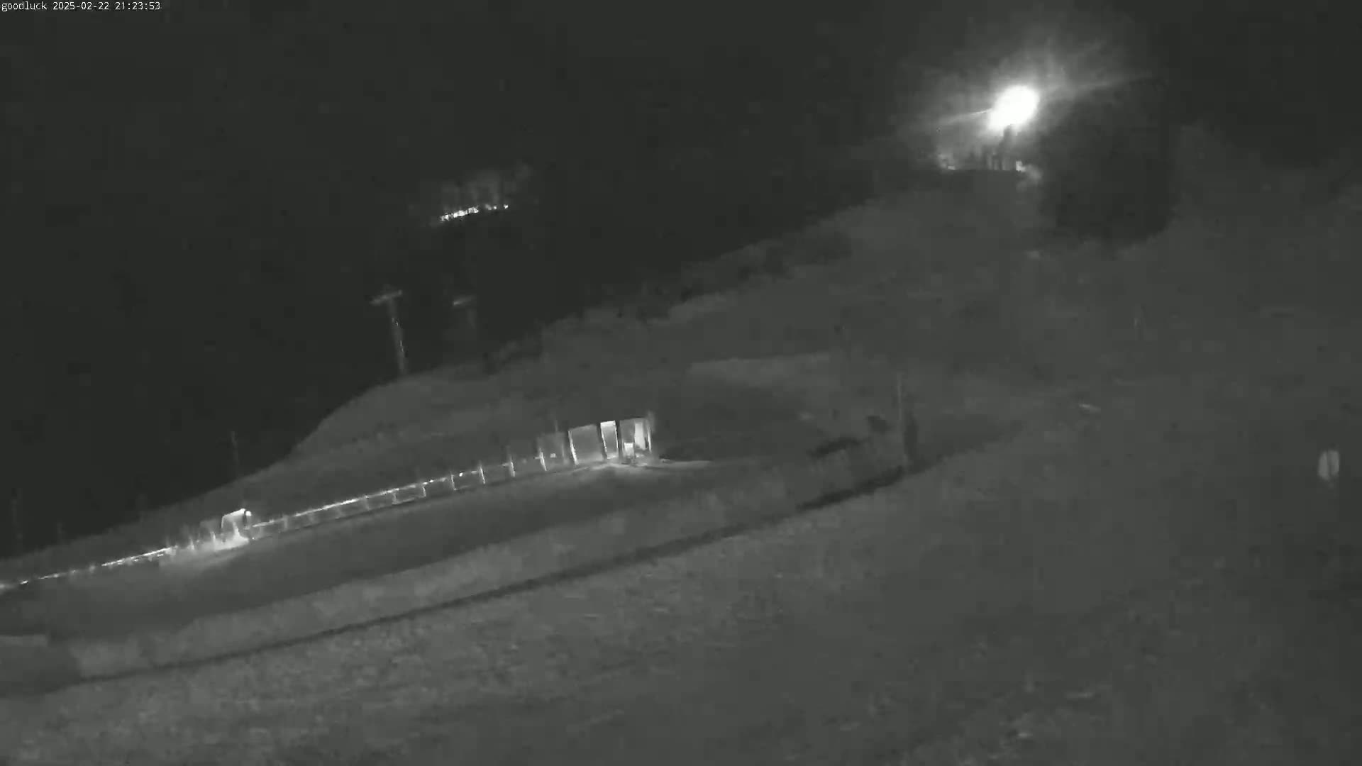A nighttime, low-light view shows a sloped, dark area with some indistinct structures and faint lights in the distance.