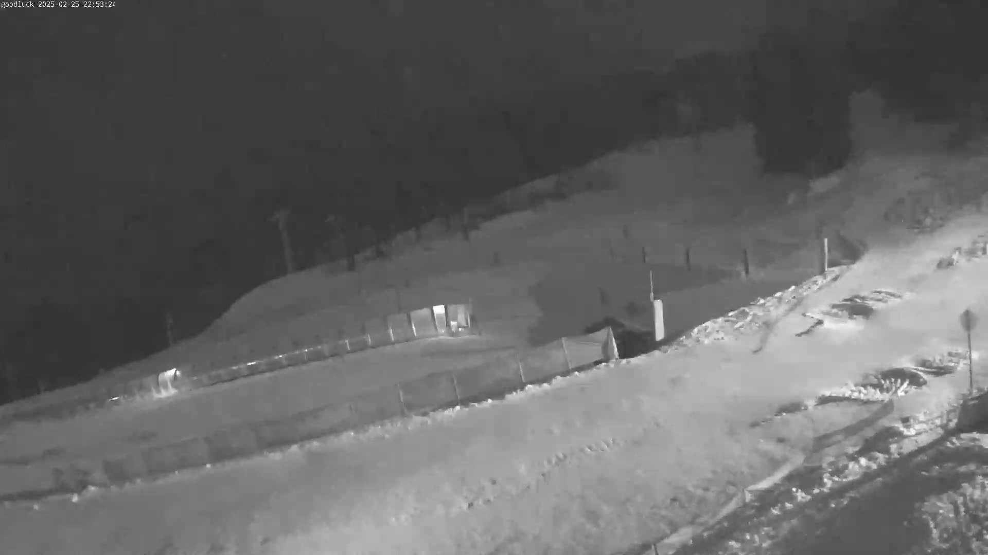 A snow-covered area at night, possibly a ski slope or toboggan run, is enclosed by a fence.