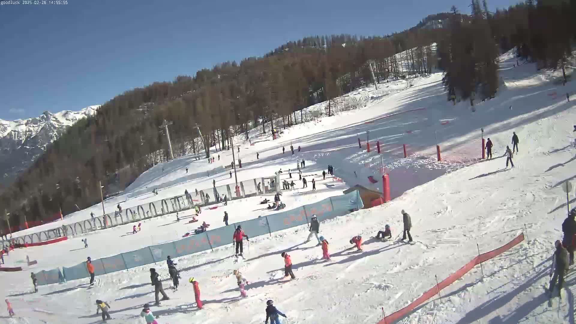A sunny day at a snow-covered ski slope shows numerous skiers and snowboarders of varying ages and skill levels enjoying the winter weather.
