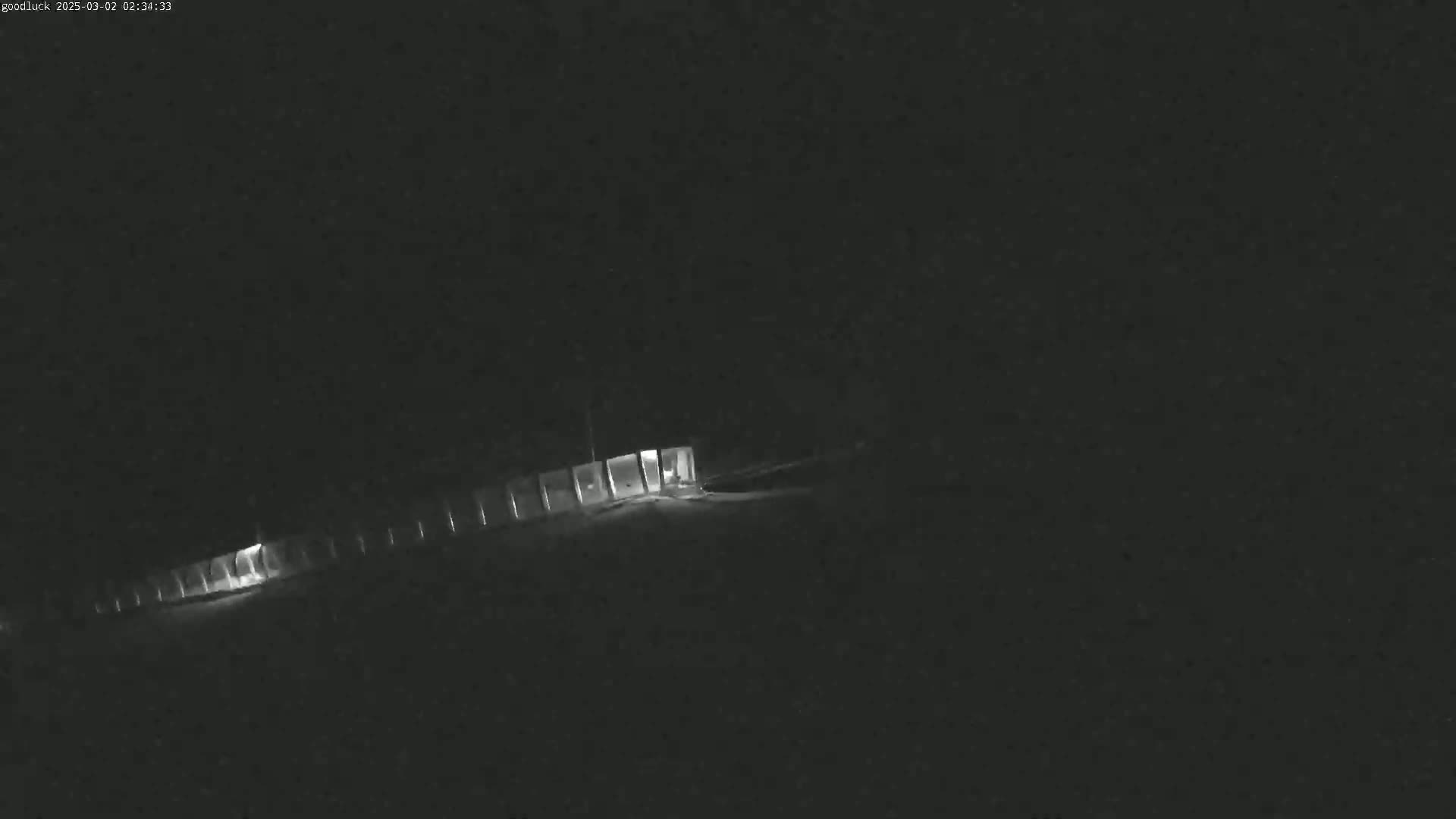 A dimly lit, long structure with evenly spaced lights is visible at night, possibly under snowy conditions.