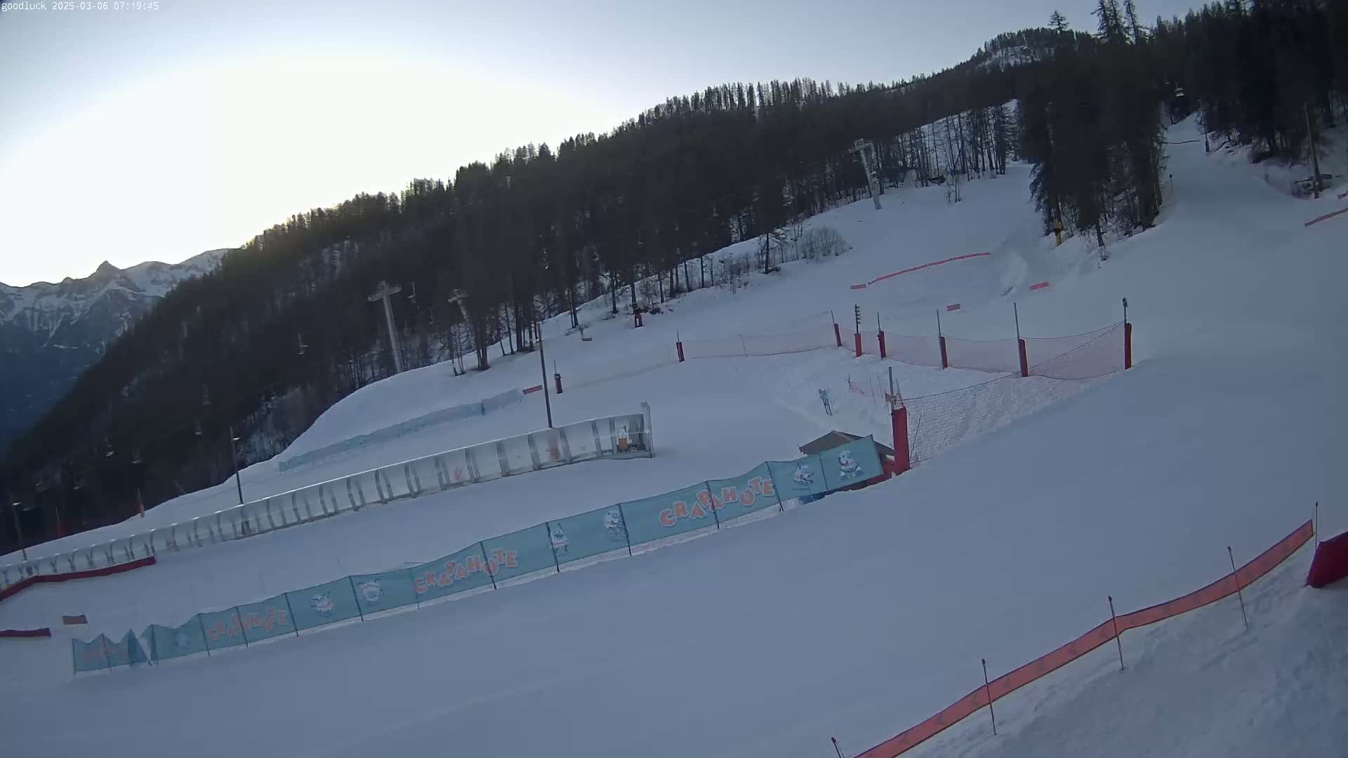 A snow-covered ski slope with ski lifts and safety nets is visible under a clear, bright sky.
