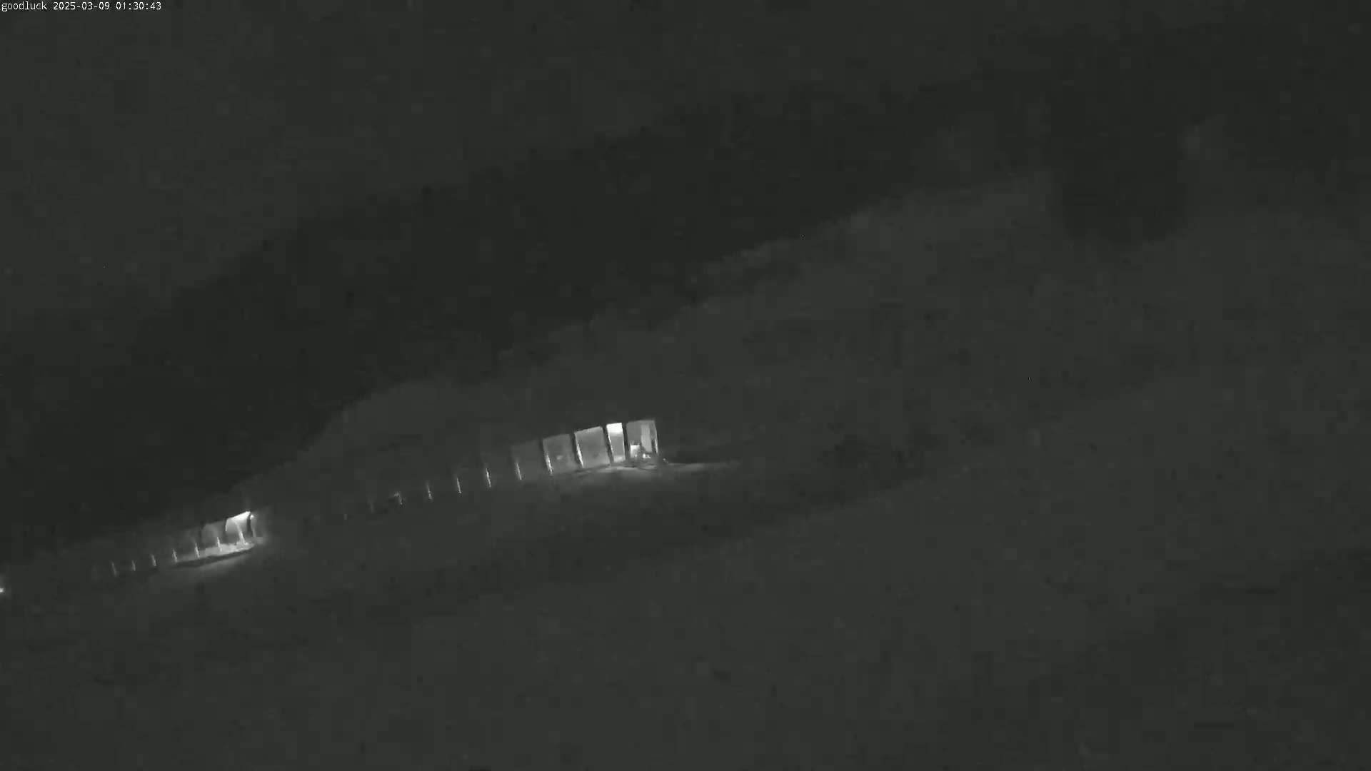 A dimly lit, long building is partially visible at night in snowy conditions.