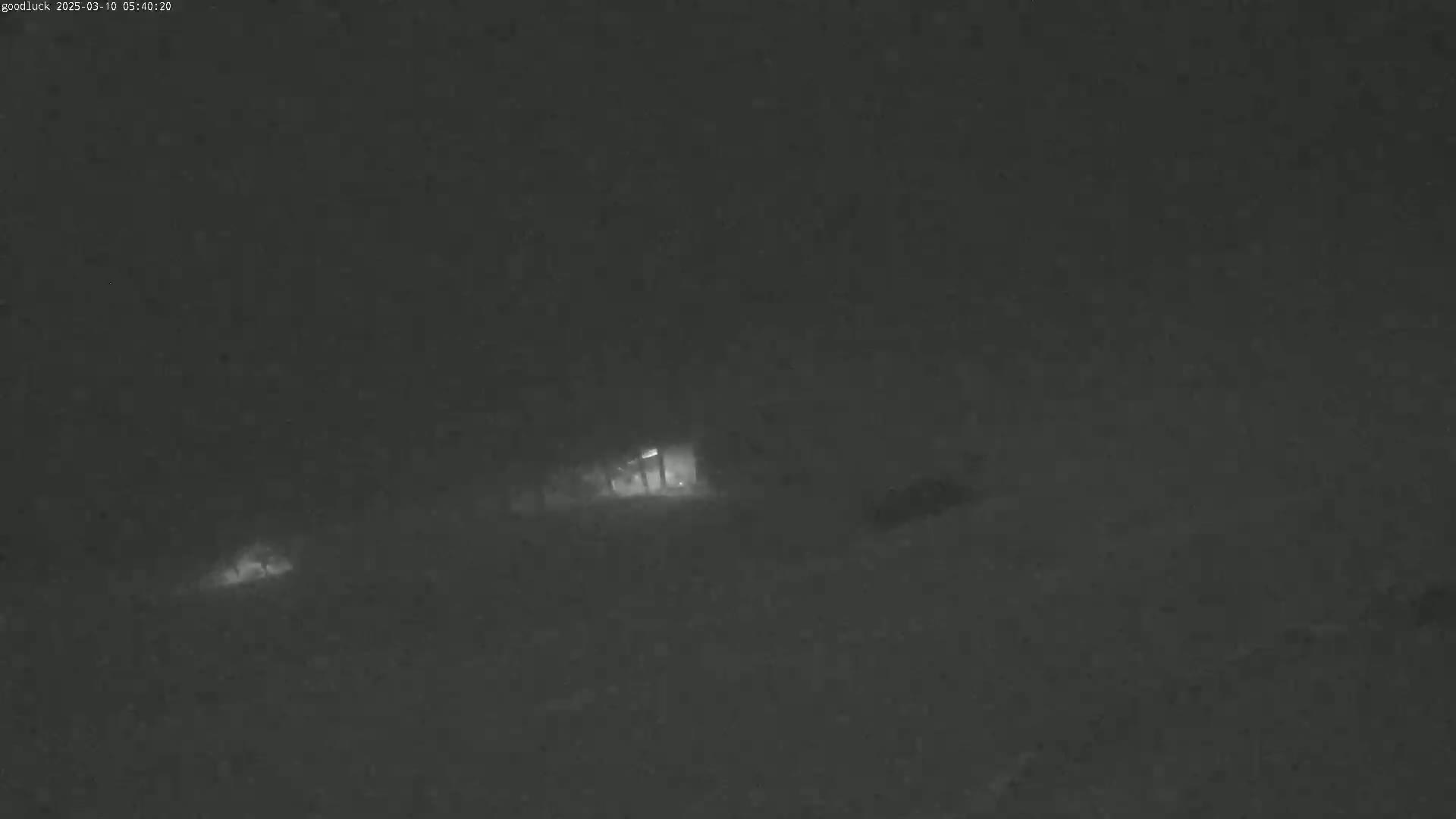 A dimly lit, snowy night scene shows a building in the distance, partially obscured by falling snow.