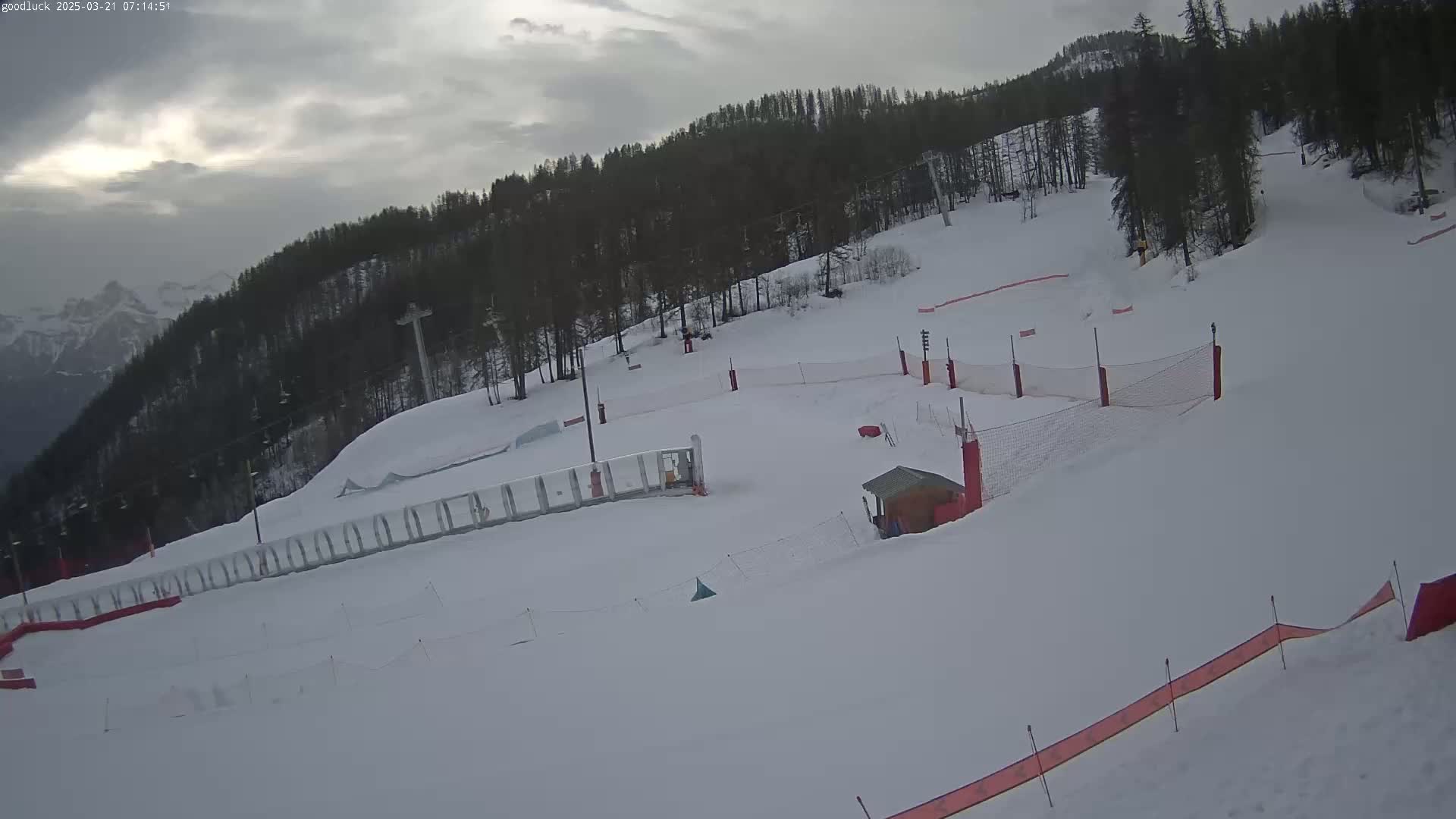 A snow-covered ski slope with a forest in the background under an overcast sky.