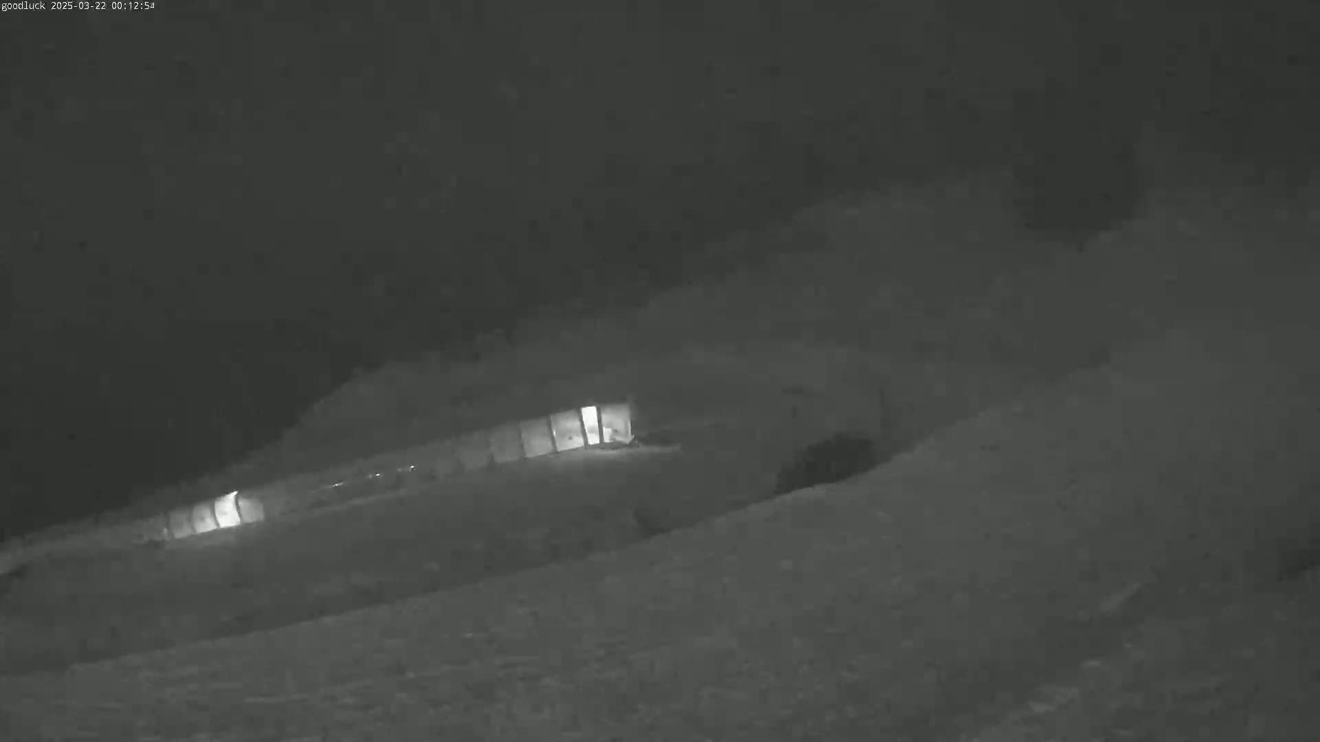 A low-light image shows a long, low building partially obscured by snow in a heavy snowstorm at night.